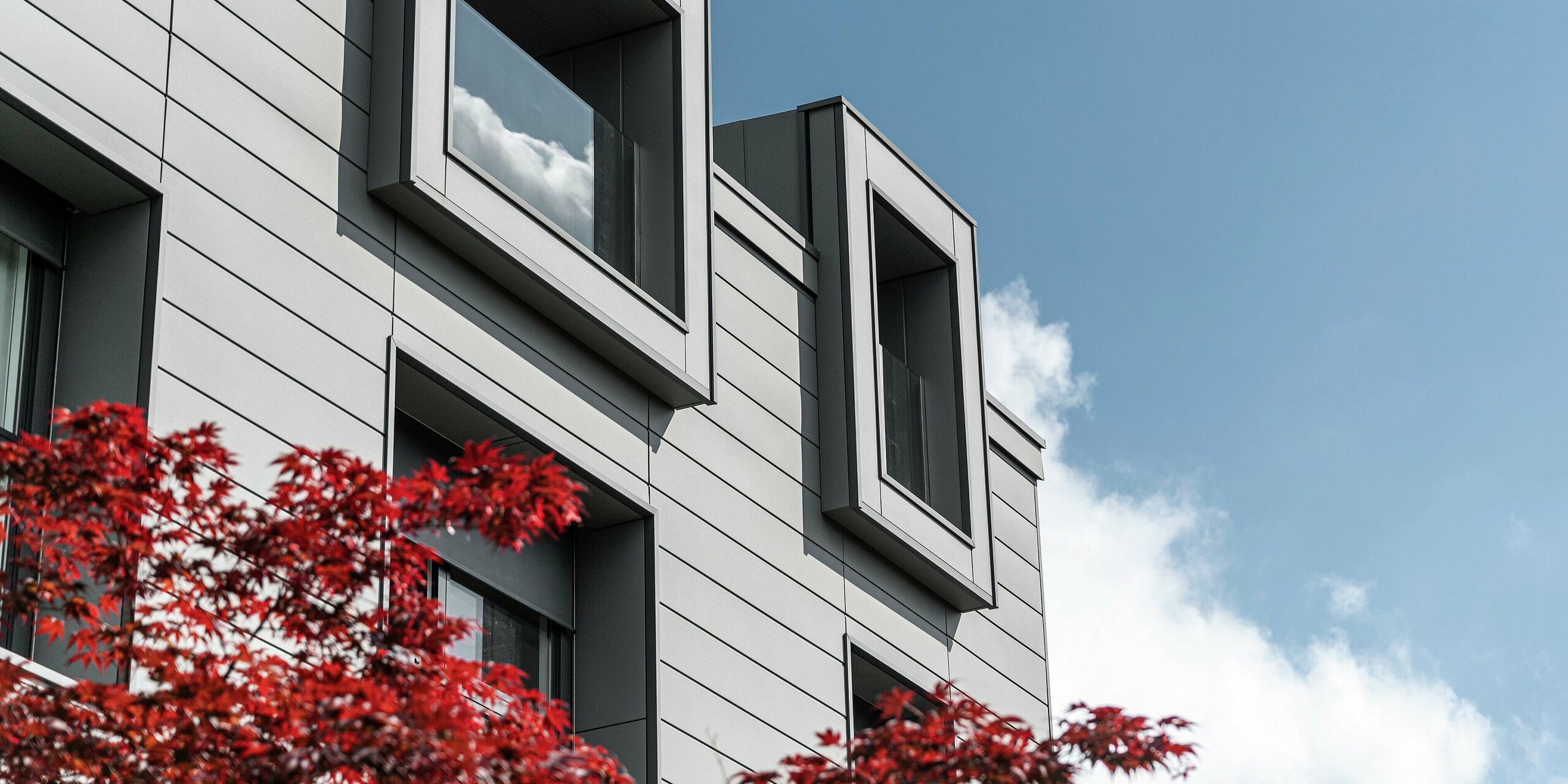 Complexe résidentiel moderne à Faloppio, en Italie, avec des fenêtres en porte-à-faux et une façade élégante en bardage PREFA. Le revêtement en aluminium offre un aspect élégant tout en offrant une grande résistance et durabilité. Un exemple réussi d'architecture fonctionnelle avec des produits PREFA de haute qualité.