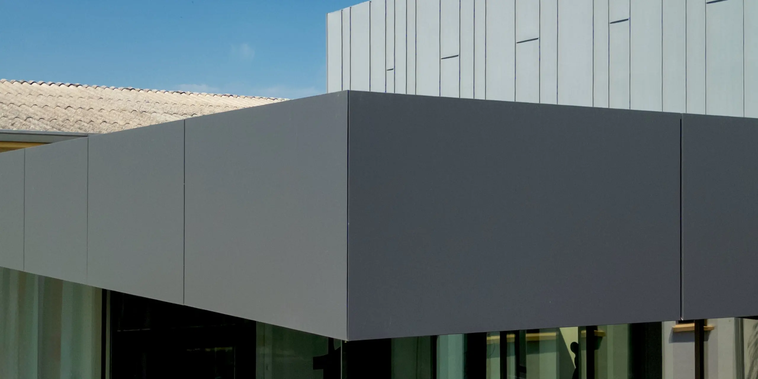 Précision et élégance se conjuguent : une projection architecturale saisissante, d'un gris sombre profond, semble flotter en apesanteur au-dessus d'une façade entièrement vitrée – un joyau architectural de la Scuola Arte e Mestieri F. Bertazzoni à Suzzara. La transition harmonieuse des couleurs, entre le volume PREFABOND plus sombre et la façade PREFALZ à la structure verticale gris quartz, crée une impression de profondeur captivante. Les produits en aluminium PREFA, d'une qualité de fabrication irréprochable, impressionnent par la précision de leurs joints, leur parfaite stabilité dimensionnelle et leur résistance durable aux intempéries – un design éducatif moderne où la qualité saute aux yeux.