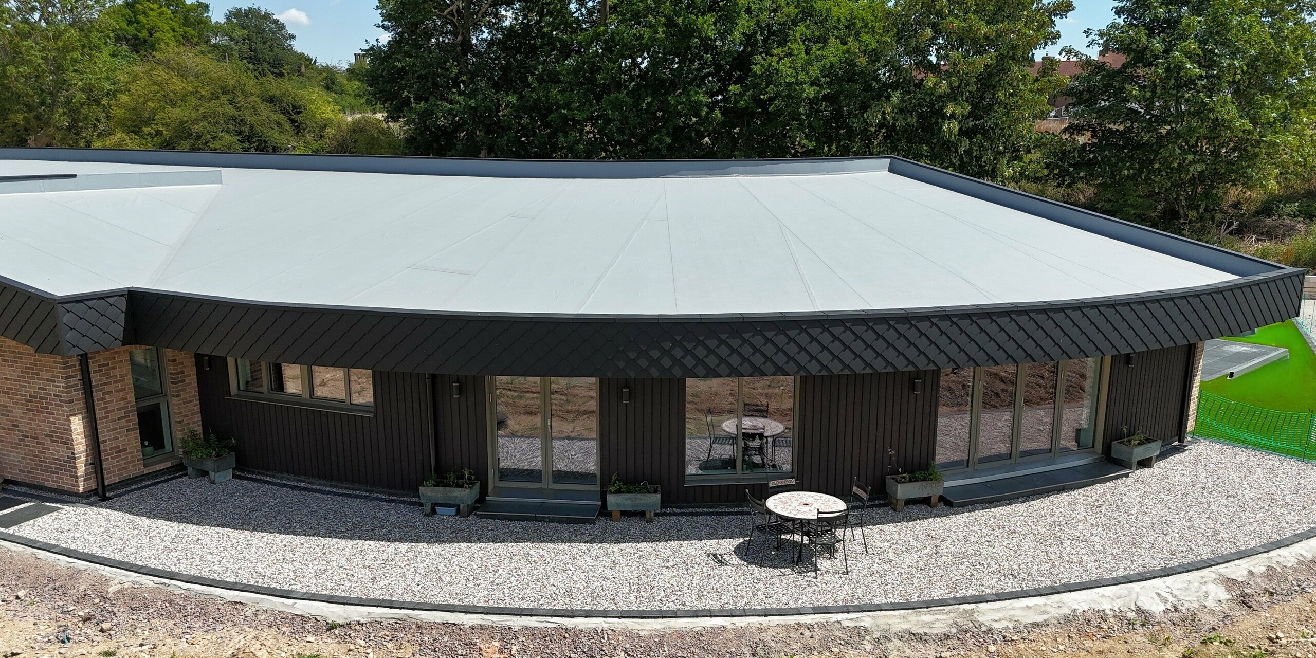 Une maison individuelle moderne au design incurvé saisissant et à la façade élégante. L'association de panneaux de bois foncé et des losanges PREFA 20 x 20 petit format, couleur anthracite P.10, confère à la façade une allure élégante et dynamique. Outre leur esthétique, les bardages en aluminium offrent des avantages tels que la durabilité, la résistance aux intempéries et la facilité d'entretien. De larges baies vitrées ouvrent l'espace de vie sur la nature, tandis que la pureté des lignes et la qualité des matériaux illustrent parfaitement une architecture durable.