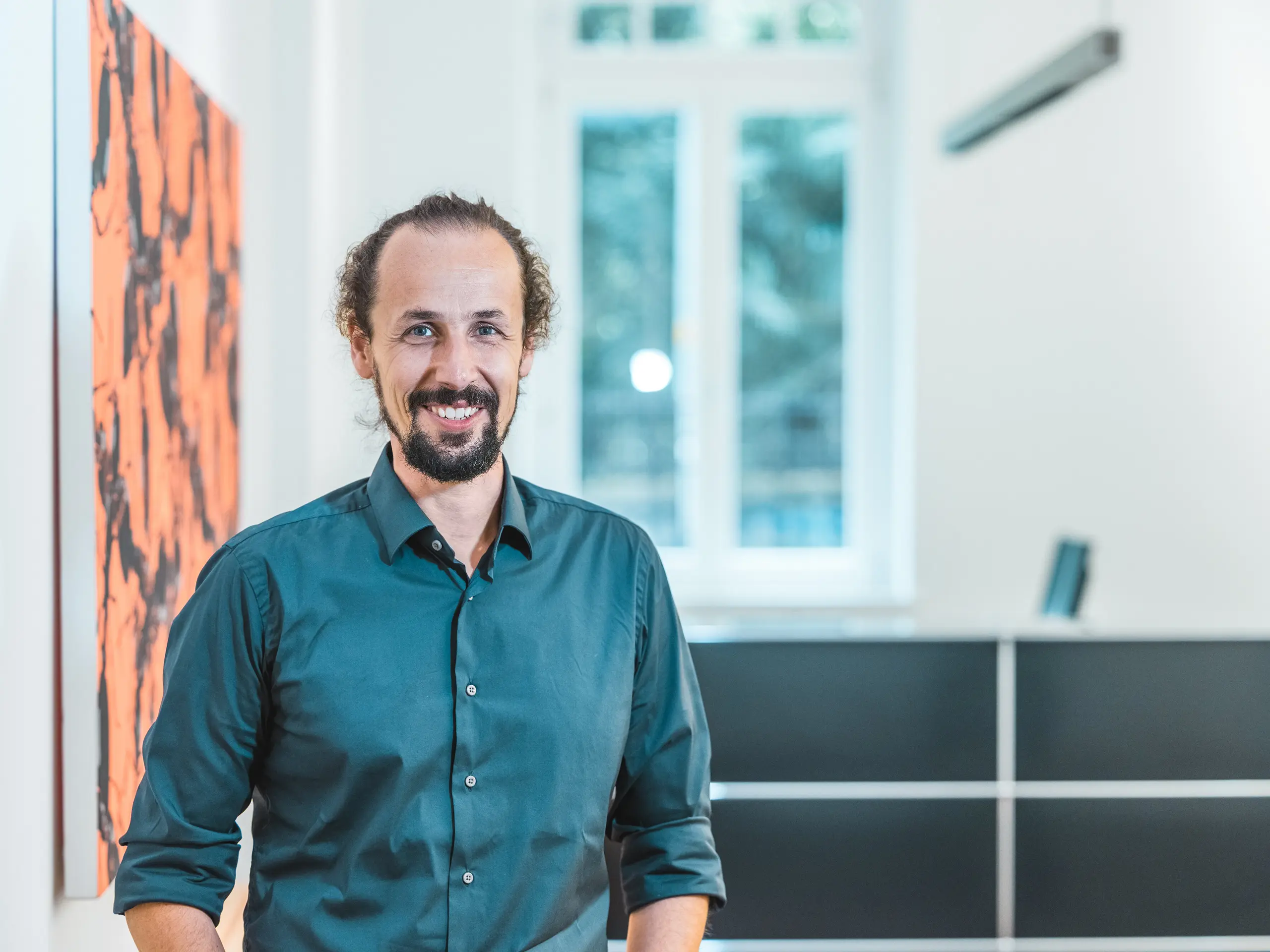 Portrait de l'architecte Gianfranco Berardesca dans un intérieur moderne. Chef de projet au sein du cabinet Höller & Klotzner Architekten, il a supervisé la réalisation du centre éducatif de Riffian, dans le Tyrol du Sud. Ce projet, mis à l'honneur par PREFARENZEN, a été conçu avec des losanges de toiture PREFA (format 44 × 44, coloris P.10 Bronze) ; il témoigne d'une planification rigoureuse, d'une grande qualité architecturale et du savoir-faire artisanal du Tyrol du Sud.