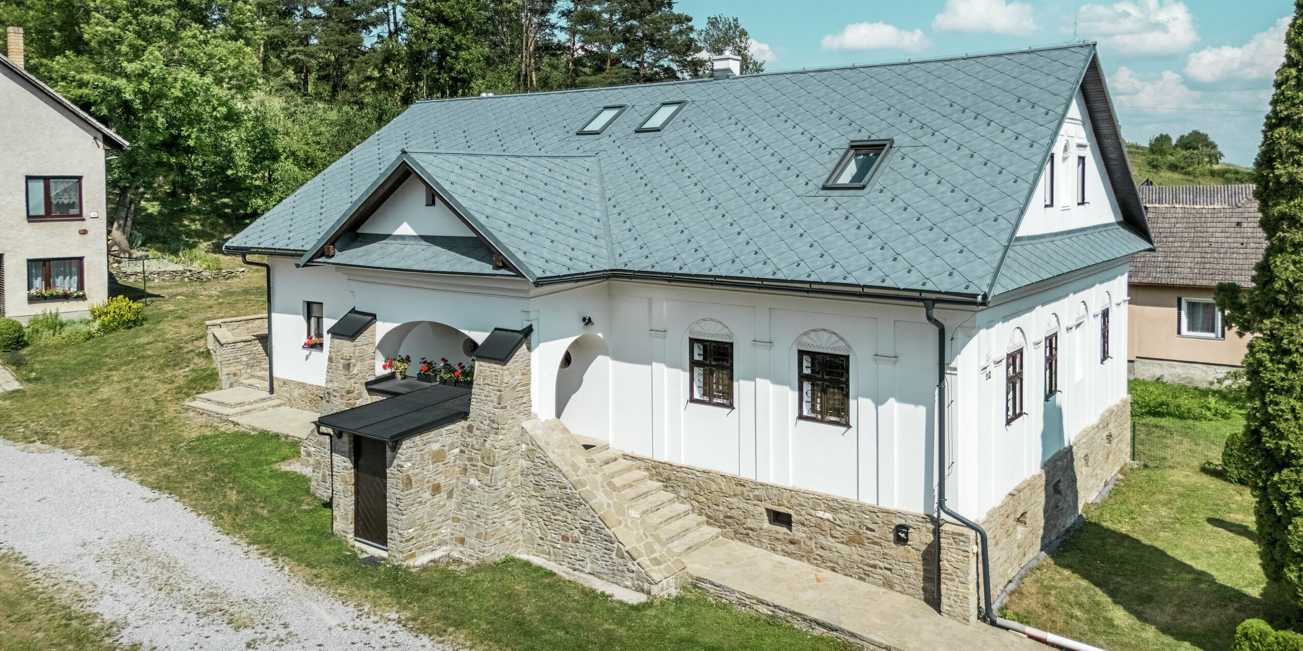 Cette magnifique maison d'artisan à Klin, en Slovaquie, arbore une toiture moderne en aluminium composée de losanges PREFA 44 x 44, couleur Gris Pierre P.10. L'élégante structure symétrique des tuiles s'harmonise parfaitement avec l'architecture classique de la maison. La toiture métallique de haute qualité, légère et durable, met en valeur la façade historique et assure une excellente résistance aux intempéries. Les puits de lumière apportent un éclairage et une ventilation supplémentaires, ajoutant une touche de modernité à ce design traditionnel. Cette solution de toiture offre non seulement des avantages esthétiques, mais aussi une solution durable et fonctionnelle pour la rénovation.