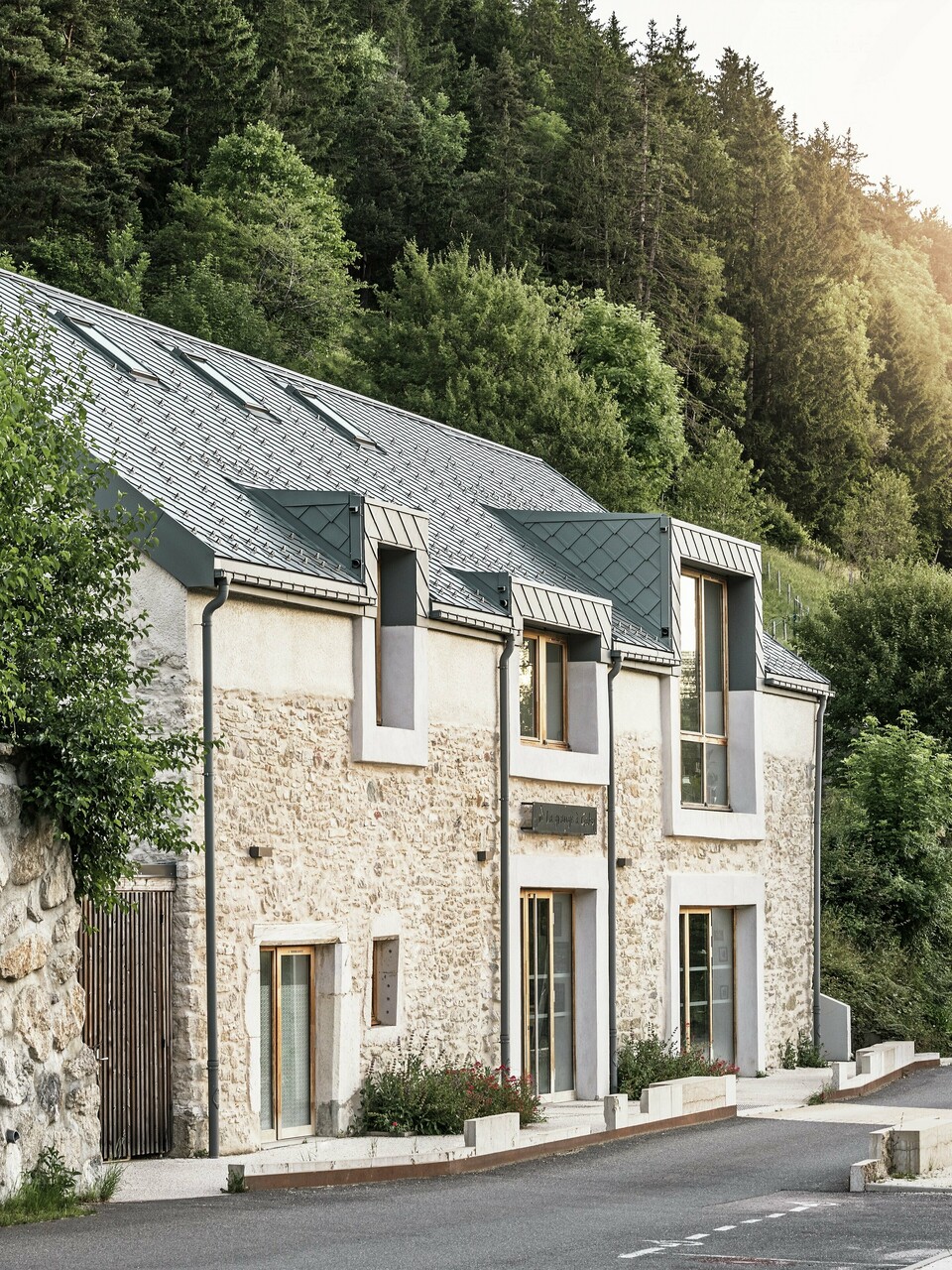 Le corps de ferme restauré "La Grange à Gaby" à Engins, France. Le bâtiment combine la maçonnerie en pierre traditionnelle avec un toit moderne en aluminium PREFA composé de losanges de toiture de 29 × 29 cm. La rénovation allie construction historique, architecture contemporaine et matériaux durables.