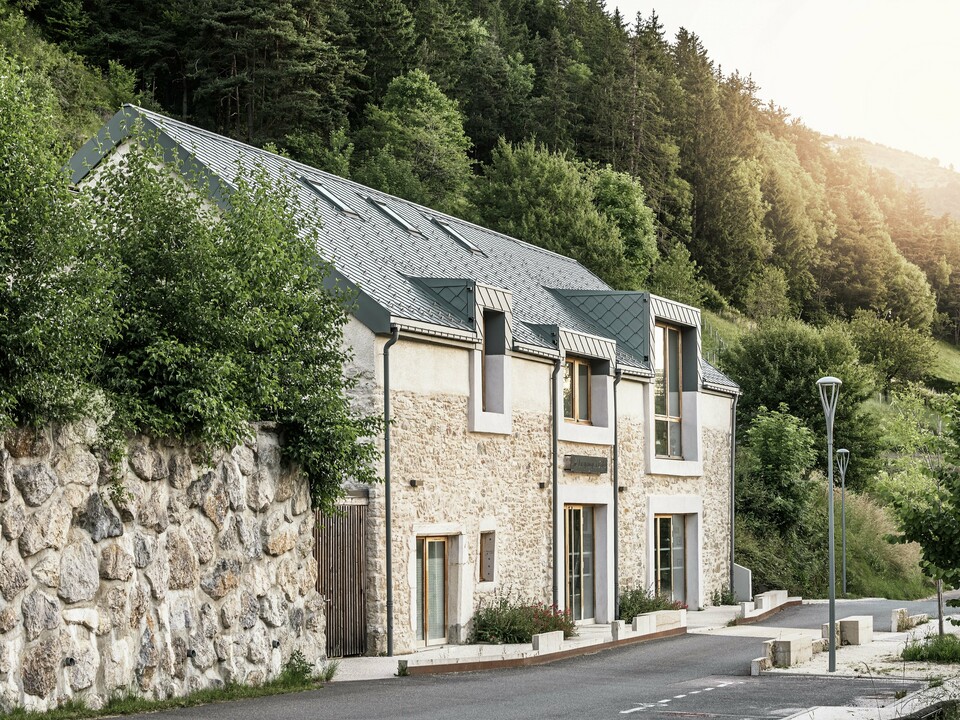 Le corps de ferme restauré "La Grange à Gaby" à Engins, France. Le bâtiment combine la maçonnerie en pierre traditionnelle avec un toit moderne en aluminium PREFA composé de losanges de toiture de 29 × 29 cm. La rénovation allie construction historique, architecture contemporaine et matériaux durables.