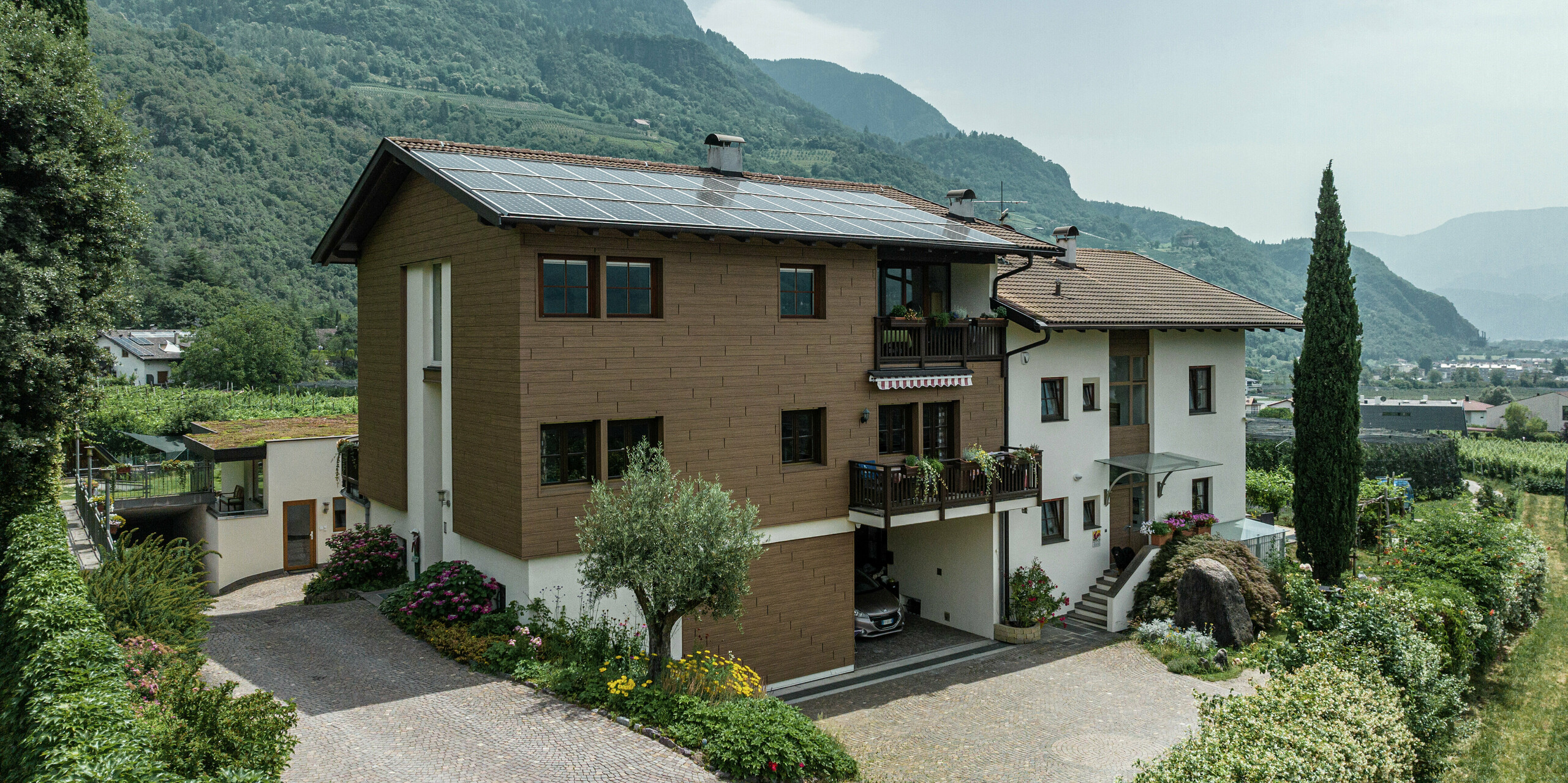 Appartements de vacances Prechtlhof rénovés à Merano, dans le Tyrol du Sud, avec Siding PREFA en noyer foncé et système photovoltaïque sur le toit. La façade en aluminium durable avec un aspect bois assure une esthétique naturelle, une durabilité maximale et un faible entretien, idéale pour l'environnement alpin.