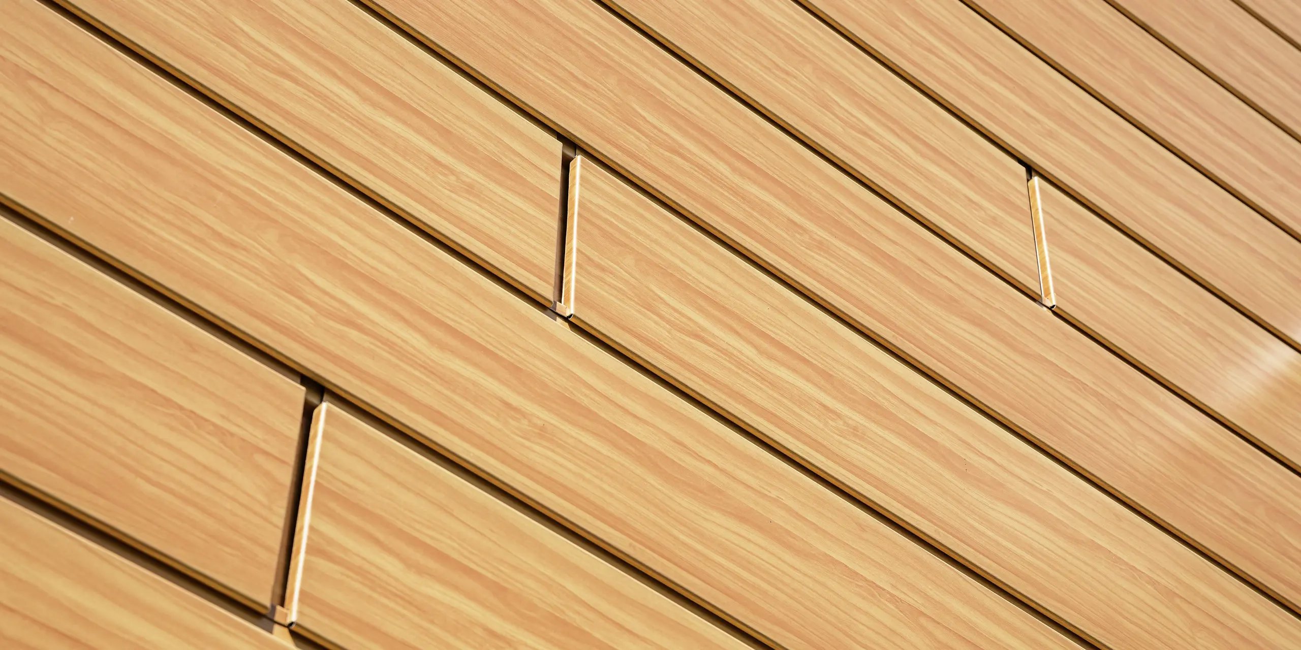 Gros plan sur les Sidings PREFA en chêne naturel. Ce revêtement en aluminium de haute qualité imite à la perfection le bois, avec un grain fin et une teinte chaleureuse. Les lignes précises des panneaux créent un effet de surface moderne et apaisant, et mettent en valeur la douce lumière. Durables, résistants aux intempéries, inaltérables et quasiment sans entretien, les bardages PREFA constituent une solution esthétique et fonctionnelle idéale pour les rénovations de façades exigeantes.Gros plan sur les Sidings PREFA en chêne naturel. Ce revêtement en aluminium de haute qualité imite à la perfection le bois, avec un grain fin et une teinte chaleureuse. Les lignes précises des panneaux créent un effet de surface moderne et apaisant, et mettent en valeur la douce lumière. Durables, résistants aux intempéries, inaltérables et quasiment sans entretien, les bardages PREFA constituent une solution esthétique et fonctionnelle idéale pour les rénovations de façades exigeantes.