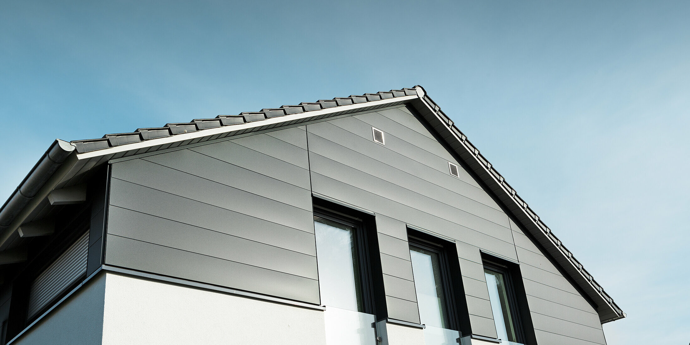 Moderne Hausfassade in Isenbüttel mit PREFA Sidings in P.10 Anthrazit – die Aluminiumverkleidung verleiht dem Einfamilienhaus einen eleganten und wetterfesten Look. Die vertikalen Fenster betonen die moderne Architektur zusätzlich.