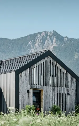 Moderner, funktionaler Wohnbau mit einer Kombination aus Holzfassade und PREFA Band- und Blechmaterial für das Dach. Die klare Architektur wird durch die elegante, metallische Dach- und Fassadenverkleidung unterstrichen, die ideal für anspruchsvolle Projekte ist. Das Bild veranschaulicht die vielseitigen Anwendungsmöglichkeiten der PREFA Produkte im Bereich Bänder und Bleche.