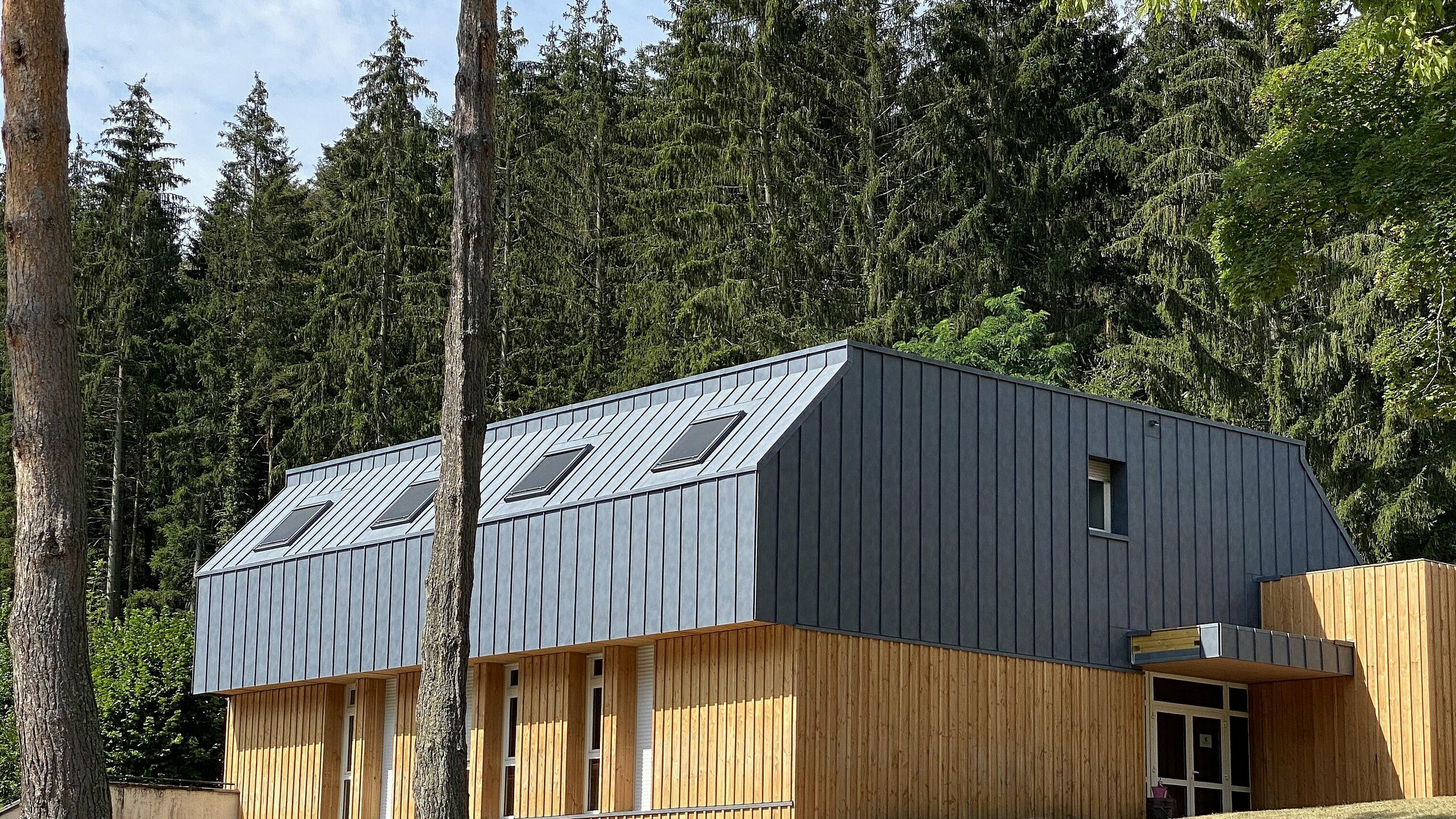 Vue éloigné du gîte l'Écrin de verdure dont la toiture et la façade ont été rénovées grâce au PREFALZ dans la teinte P.10 gris pierre