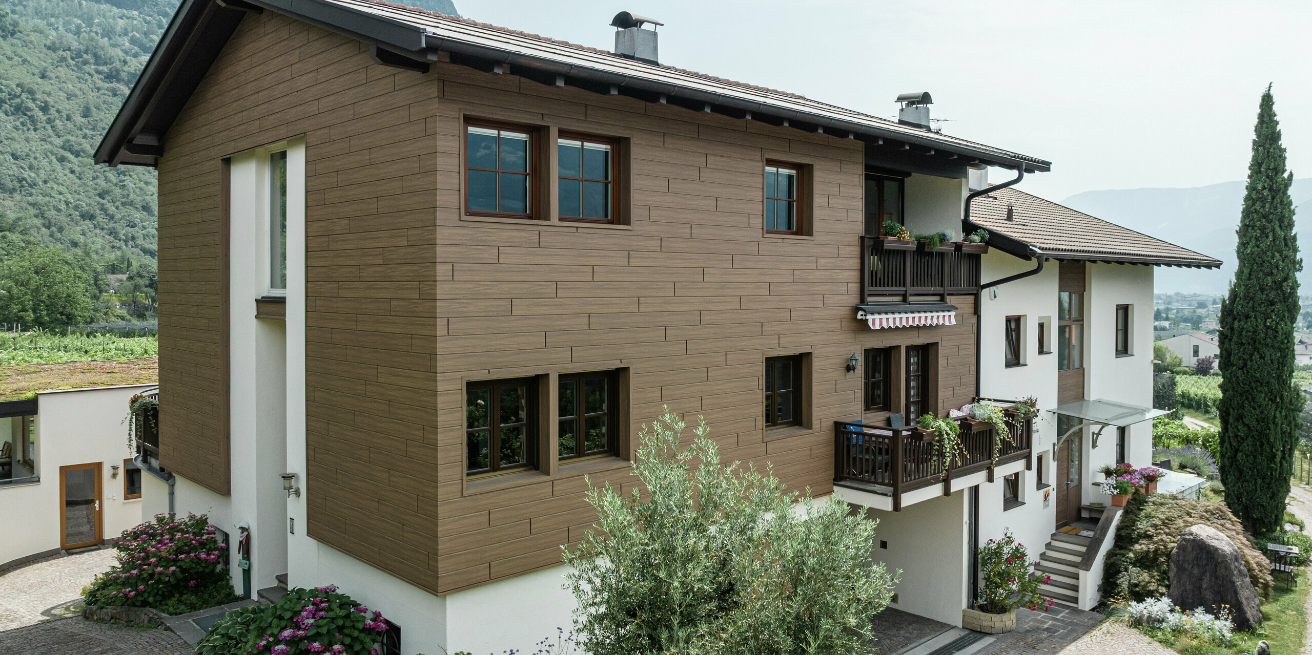 Les appartements de vacances modernisés Prechtlhof à Merano, dans le Tyrol du Sud, avec une façade PREFA durable en noyer foncé. Le Siding en aluminium aspect bois allie une esthétique traditionnelle à une durabilité sans entretien et s'intègre harmonieusement dans le paysage alpin.