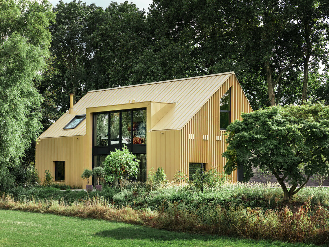Vue latérale de la maison individuelle à Elst (NL) couverte par PREFA. Des buissons et des arbres entourent le bâtiment.
