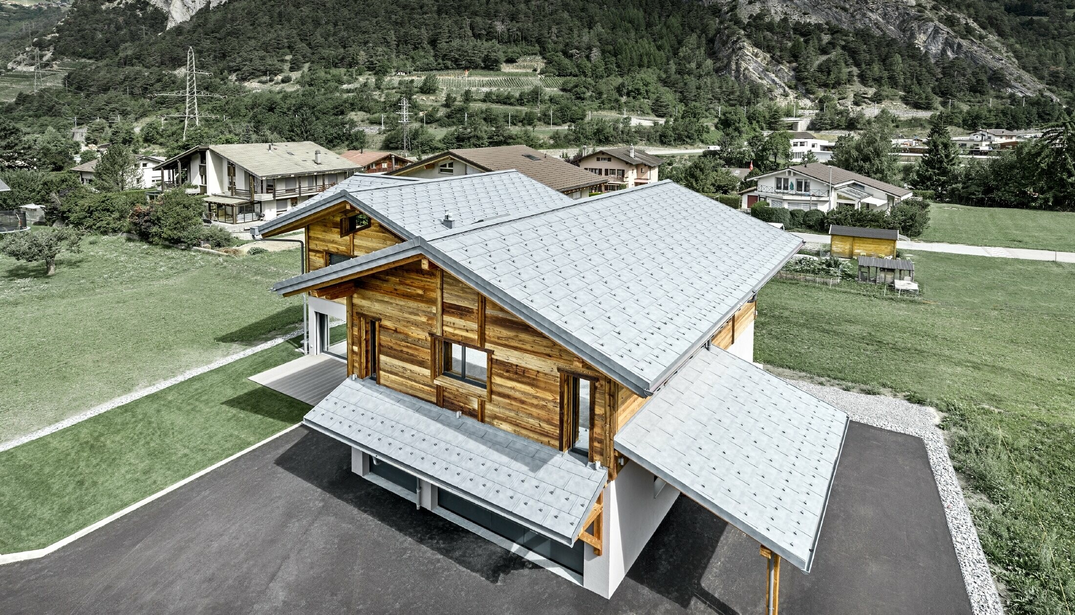 Vue aérienne du chalet Fabrice ; le chalet a été recouvert de tuiles R.16 PREFA couleur gris pierre avec arrêts neige, la partie haute du bâtiment est habillée avec une façade en bois rustique.