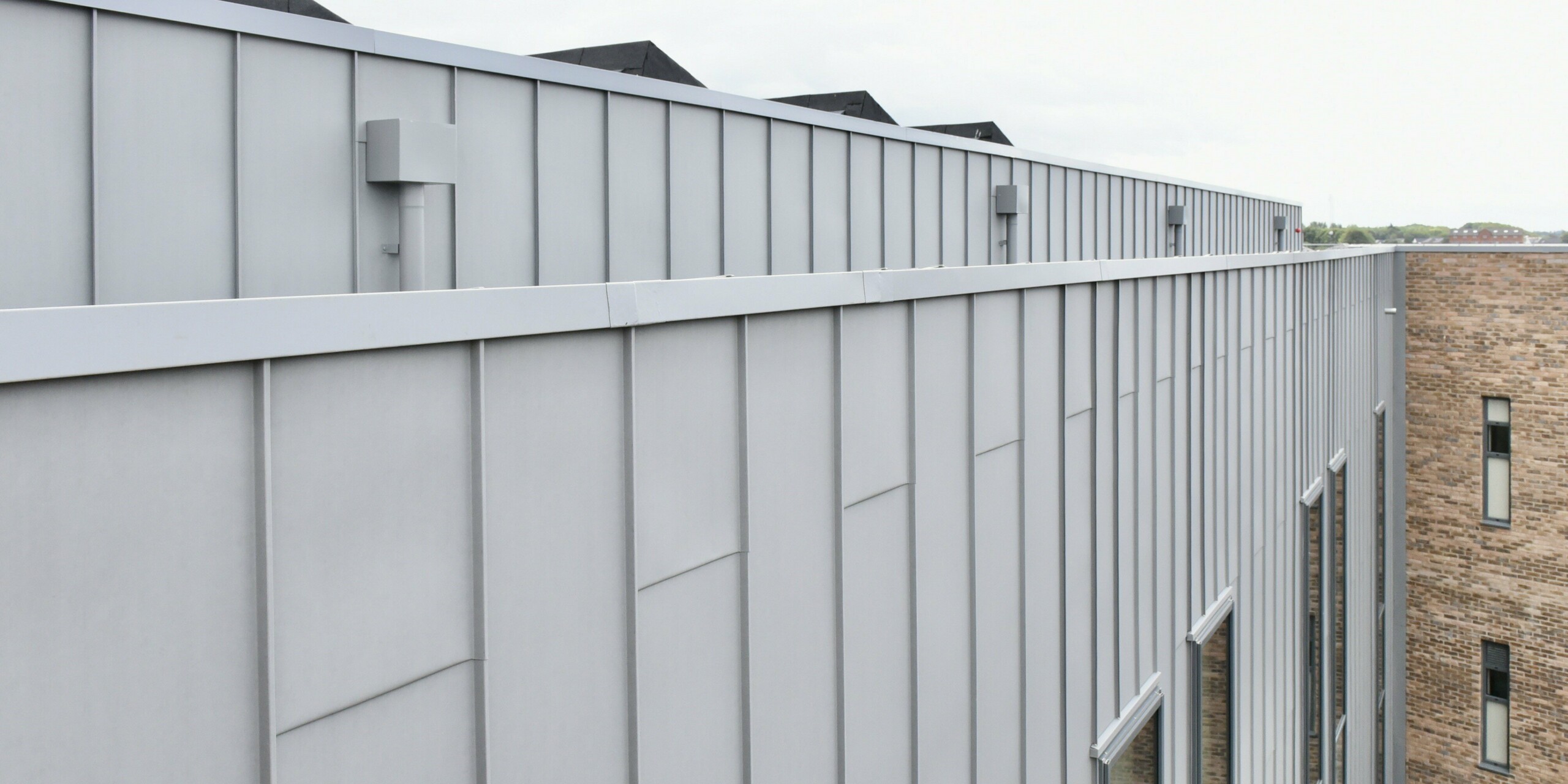 Vue détaillée de la façade en aluminium PREFALZ en gris quartz au Regional College North, Royaume-Uni. Les lignes claires et l'aspect mat du revêtement à joint debout soulignent la finition de haute qualité et le design intemporel.