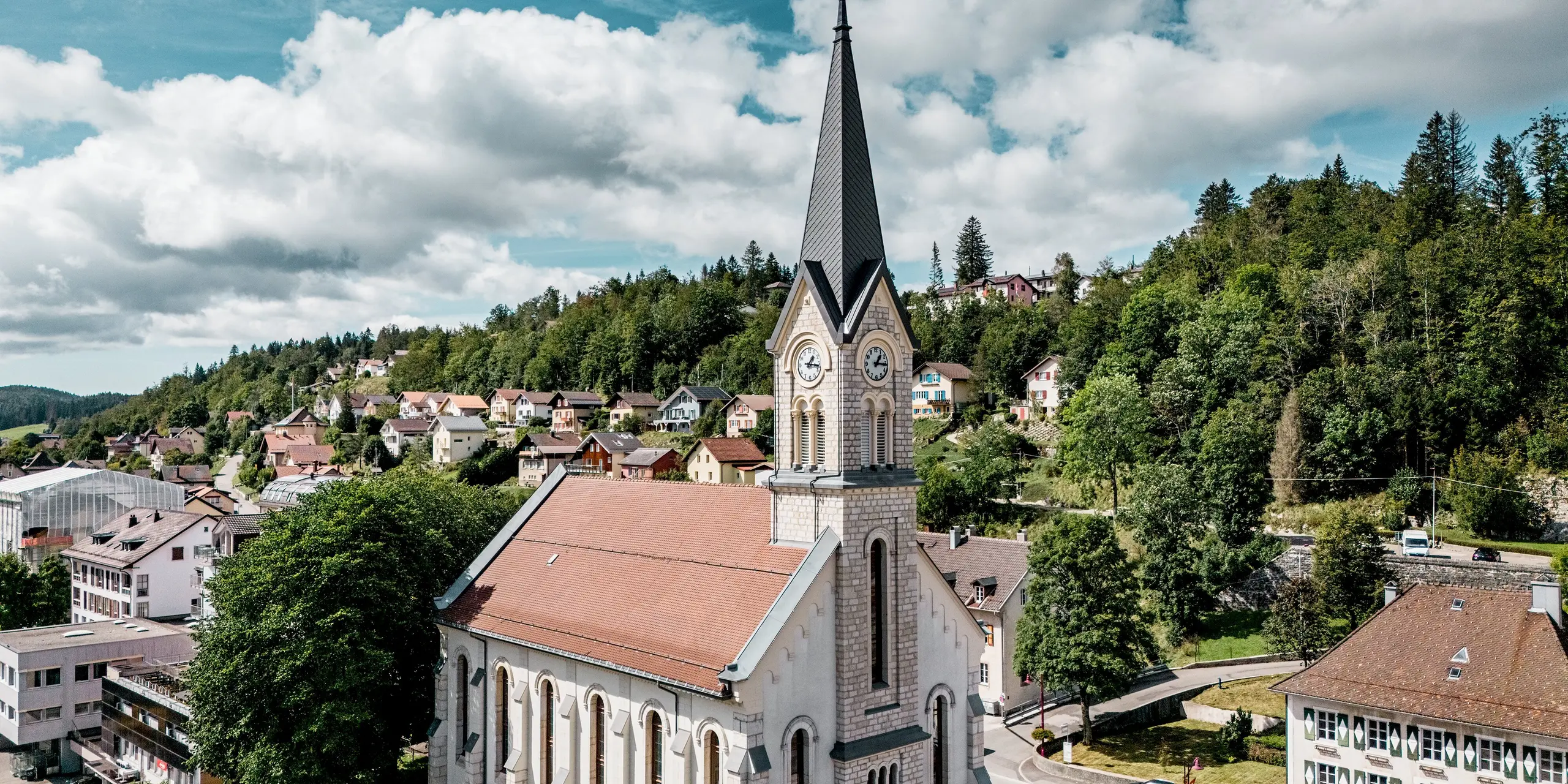 Église historique du Sentier, en Suisse, avec une flèche remarquable réalisée en losanges PREFA 29 x 29 cm, coloris Gris sombre P.10. La robuste toiture en aluminium crée un contraste saisissant avec la pierre naturelle claire et sculpte avec élégance le paysage urbain. L'aluminium PREFA est reconnu pour sa durabilité, sa légèreté et sa grande résistance, même sur des toitures aux géométries complexes.