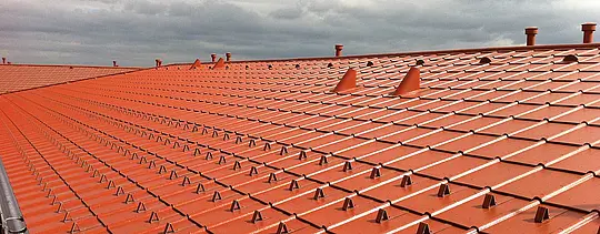 Gros plan d’un toit PREFA en aluminium imitation tuile – Tuiles PREFA rouge tuile avec arrêts de neige