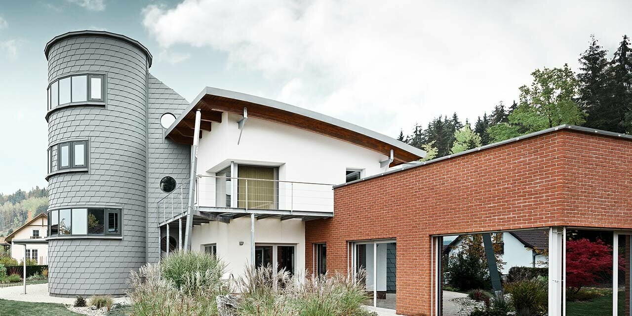 Maison individuelle avec extension de tour ; la tour ronde est revêtue du bardeau de façade PREFA couleur gris quartz 