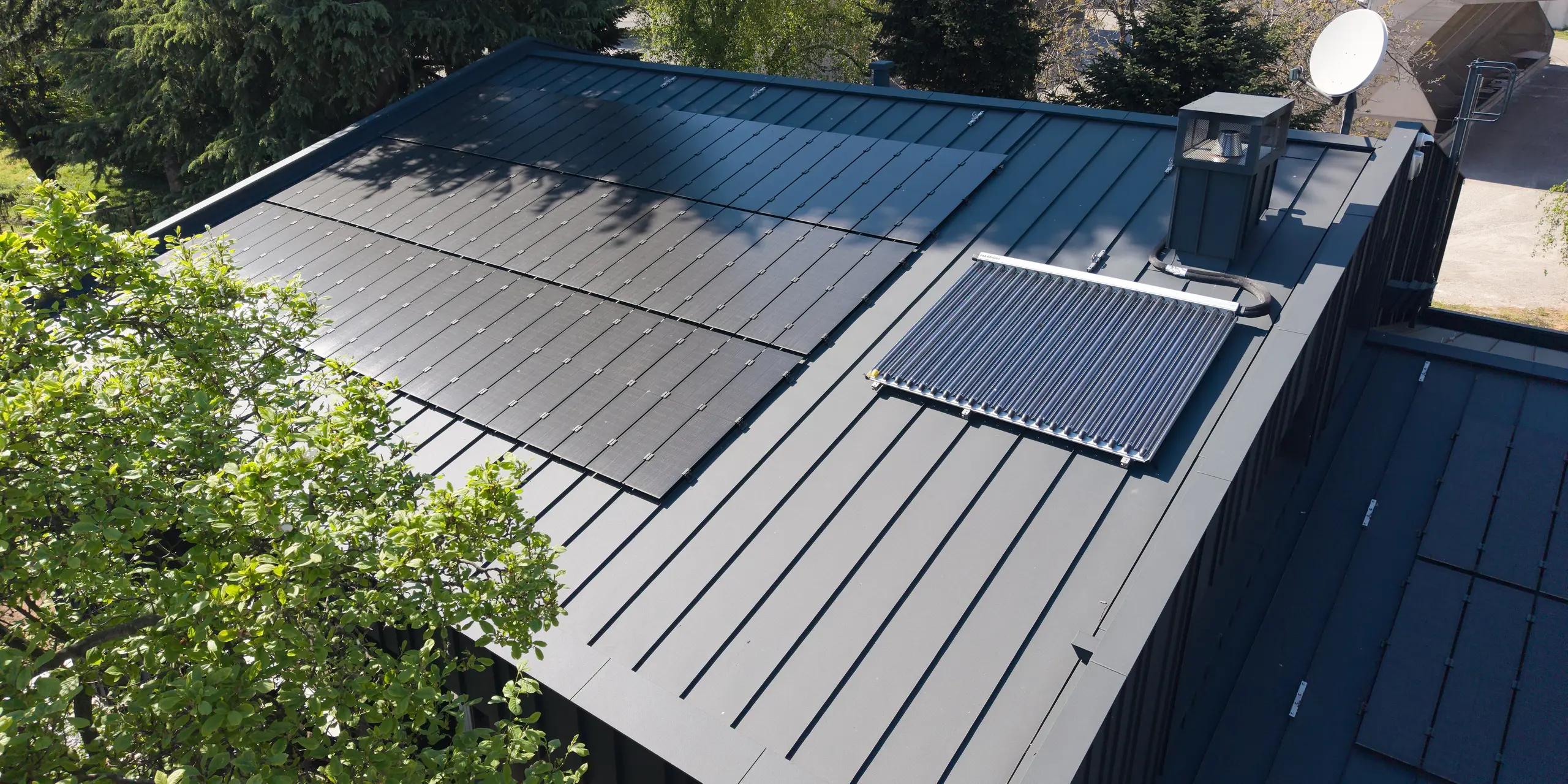 Vue aérienne de la toiture moderne en aluminium PREFALZ de la Villa Castellanza, P.10 Anthracite. Les modules solaires PREFALZ, parfaitement intégrés, constituent l'élément central et allient esthétique et production d'énergie durable. La netteté des joints, la qualité et la durabilité des matériaux PREFALZ, ainsi que l'intégration harmonieuse dans l'environnement verdoyant, contribuent à l'impression architecturale générale remarquable.