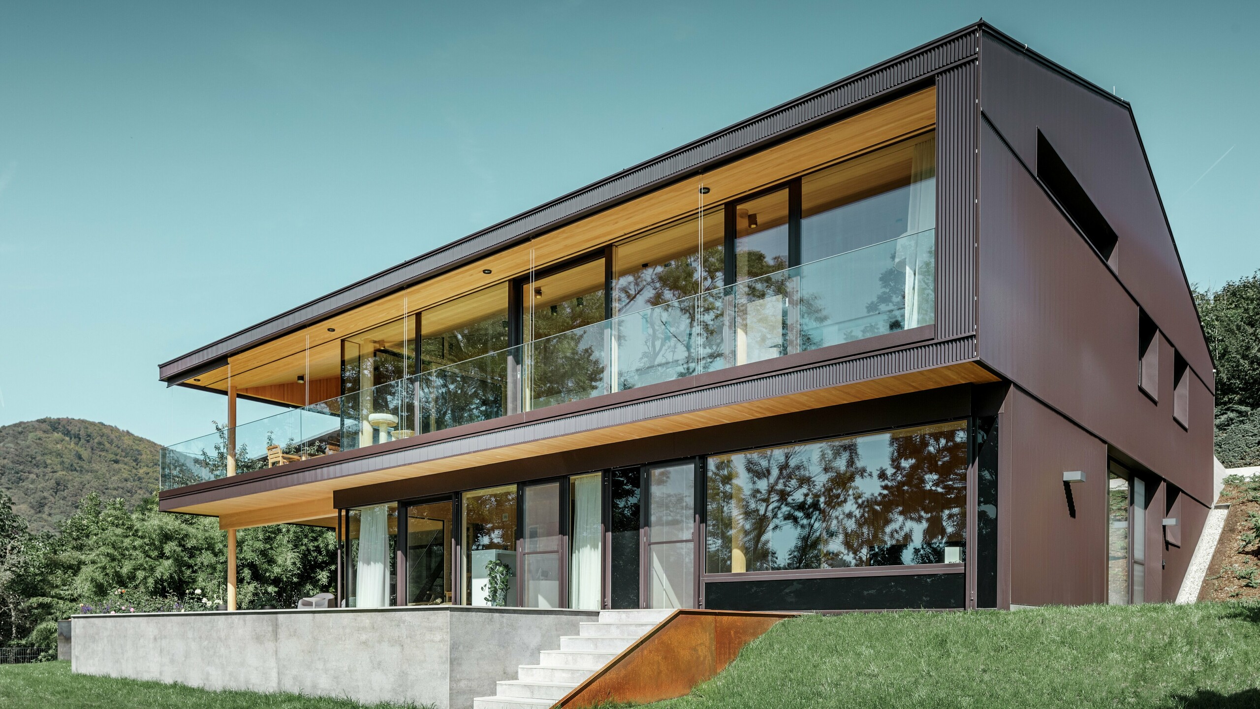 Maison individuelle moderne à grandes fenêtres côté jardin, dont la façade a été recouverte de profils triangle PREFA couleur brun foncé.