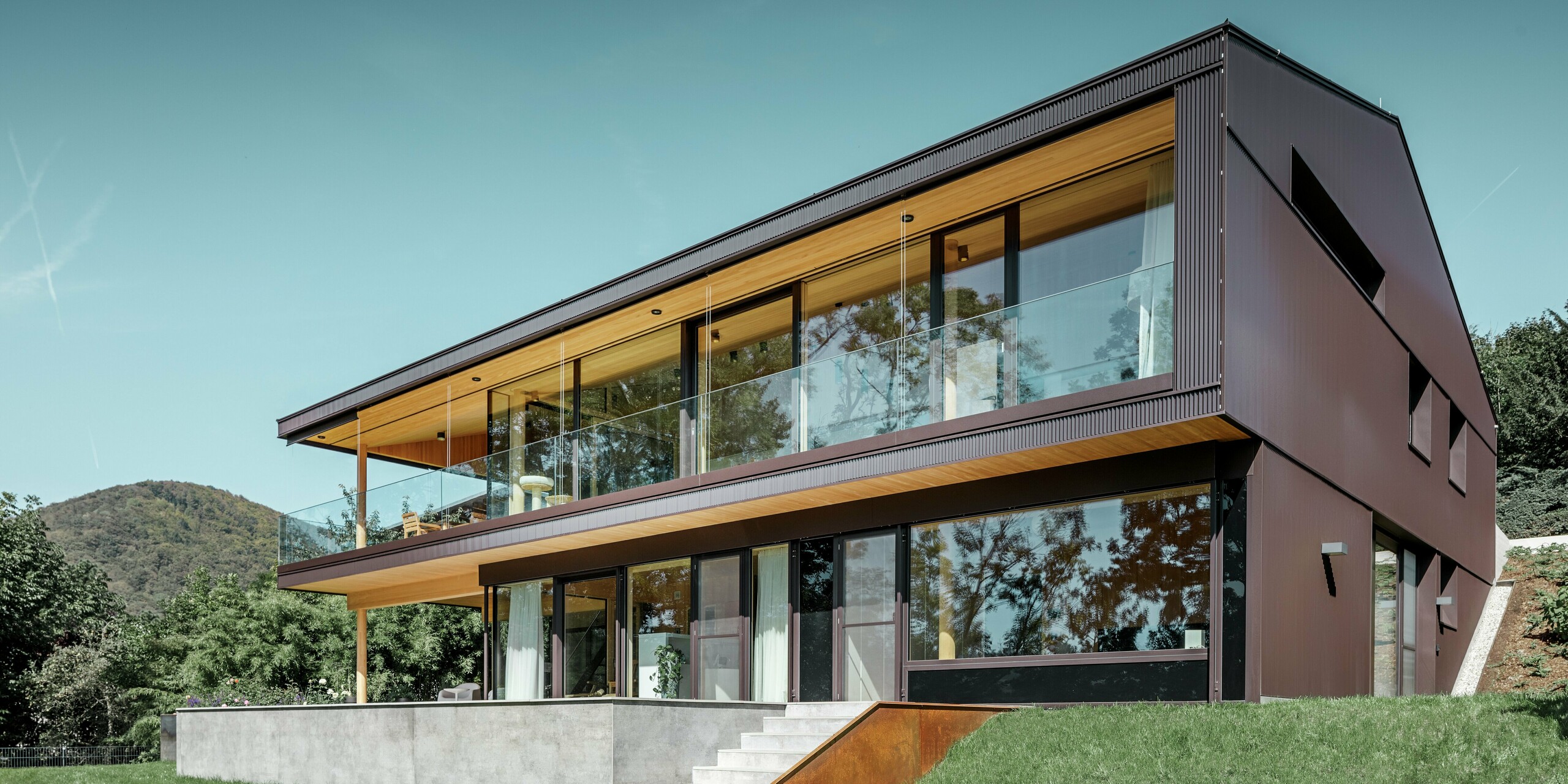 Maison individuelle moderne à grandes fenêtres côté jardin, dont la façade a été recouverte de profils triangle PREFA couleur brun foncé.
