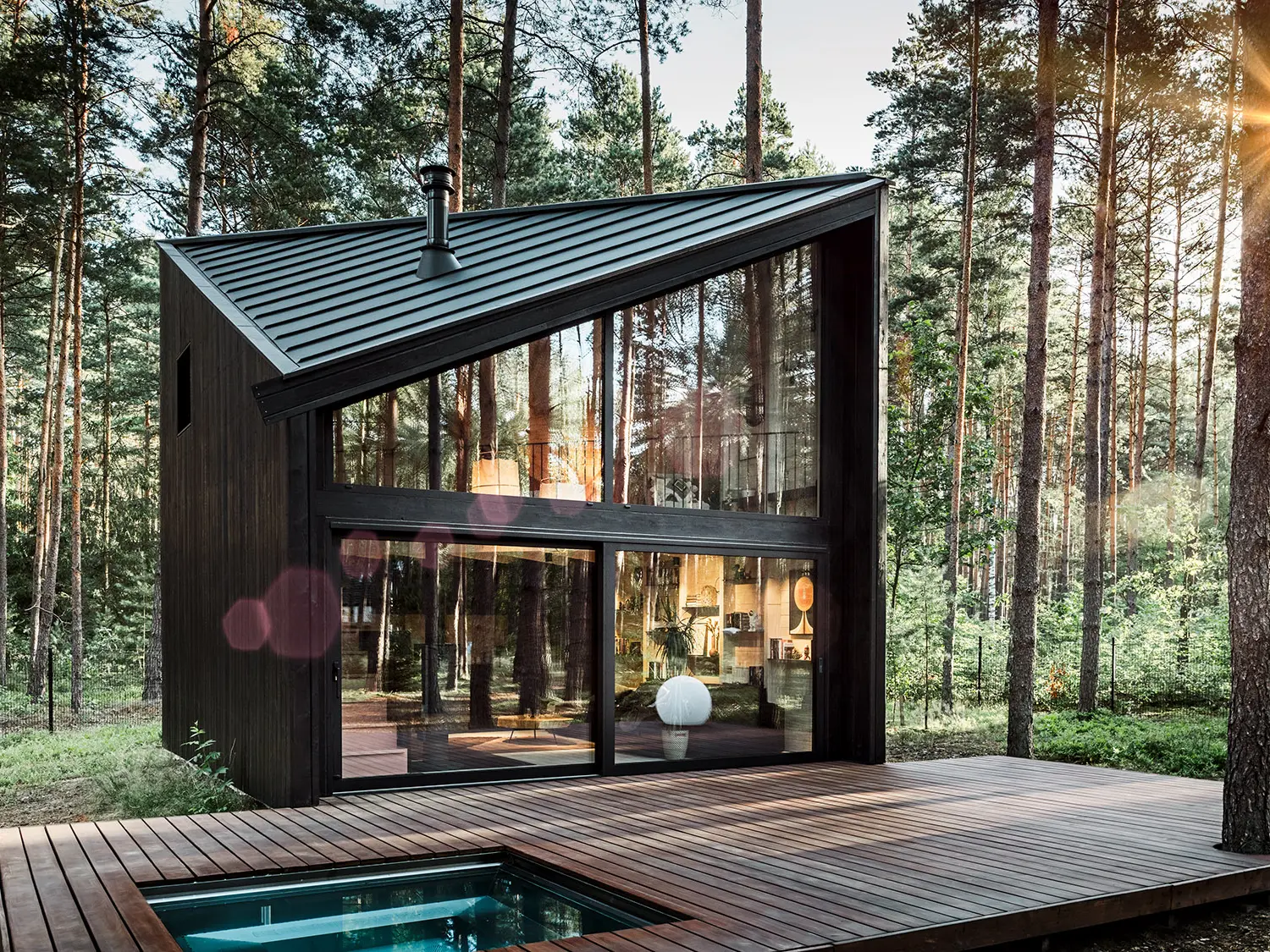 Vue latérale d'une maison de vacances avec un toit en PREFALZ en pente. La nature environnante se reflète dans la zone vitrée.