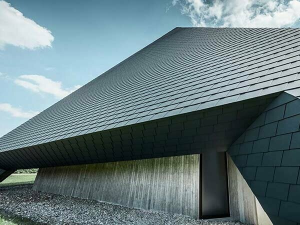 Neu saniertes Dach der Kirche Langenau mit anthrazitfarbigen, sturmsicheren Dachschindeln aus Aluminium von PREFA, das Dach zieht sich vom Boden durch bis zur Spitze ähnlich einer dunkelgrauen Pyramide