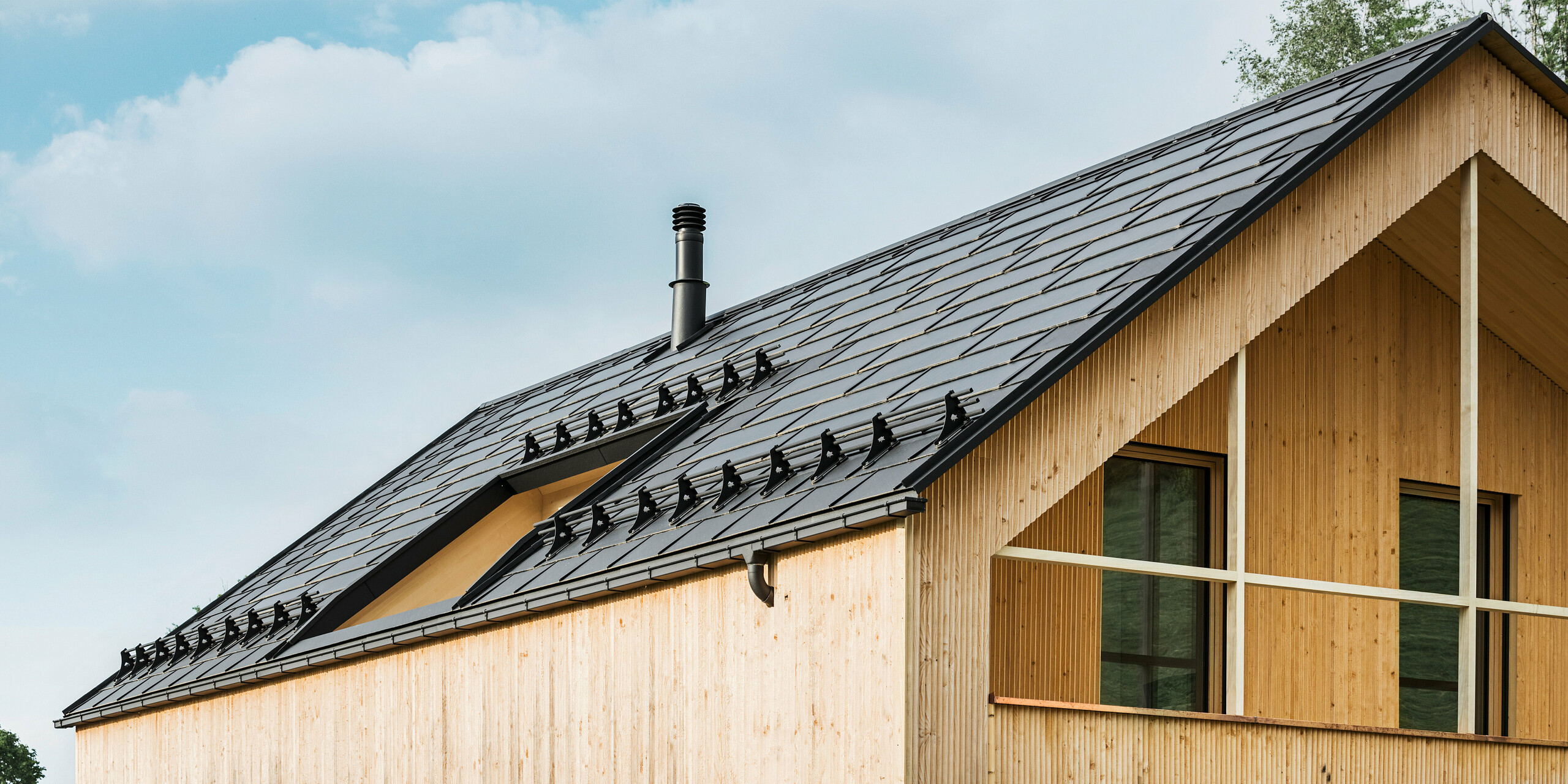 Maison individuelle dans la ville autrichienne d'Egg avec le panneau de toit solaire PREFA et le panneau de toit R.16 en noir, combinés à une façade en bois
