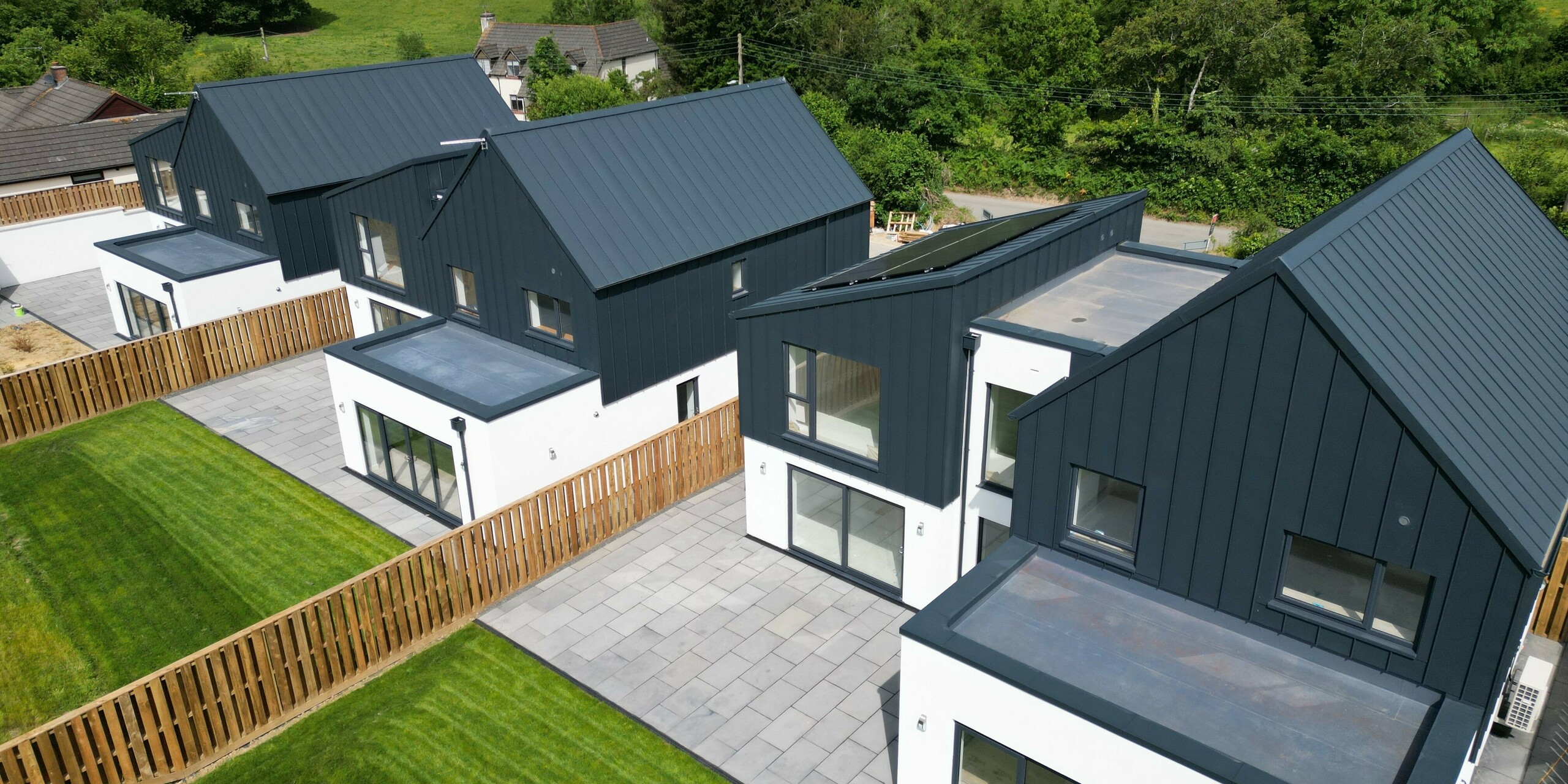 Vue latérale de trois des cinq maisons individuelles de Bridgerule, Devon, avec toiture PREFALZ et façade en P.10 Anthracite. Le revêtement en aluminium durable souligne le caractère moderne et résistant aux intempéries du bâtiment - idéal pour une construction durable.