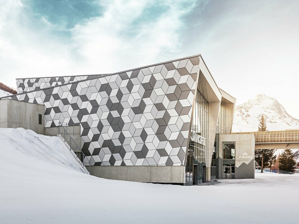 La station aval des Deux Alpes impressionne par sa façade exceptionnelle en panneaux composites en aluminium PREFABOND au motif losanges moderne. L'association de tons blancs et gris crée un design saisissant qui s'harmonise parfaitement avec le paysage montagneux enneigé. Cette façade durable et résistante aux intempéries garantit une solution esthétique et fonctionnelle, même dans des conditions extrêmes. Le soleil éclatant en arrière-plan crée un décor majestueux.