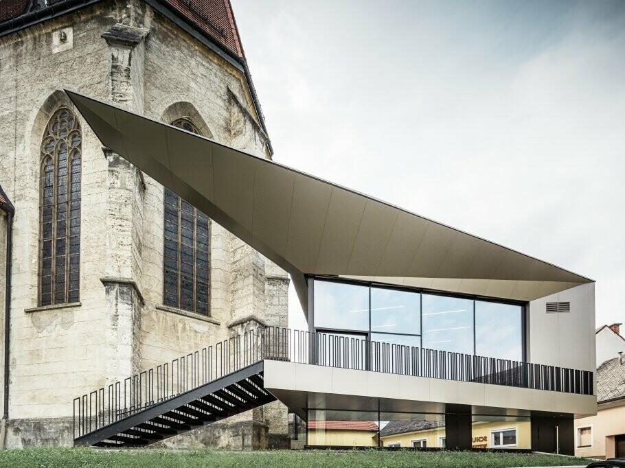 Vue latérale du centre paroissial FOKUS avec les panneaux de façade PREFA et une église à Sierning (Autriche).