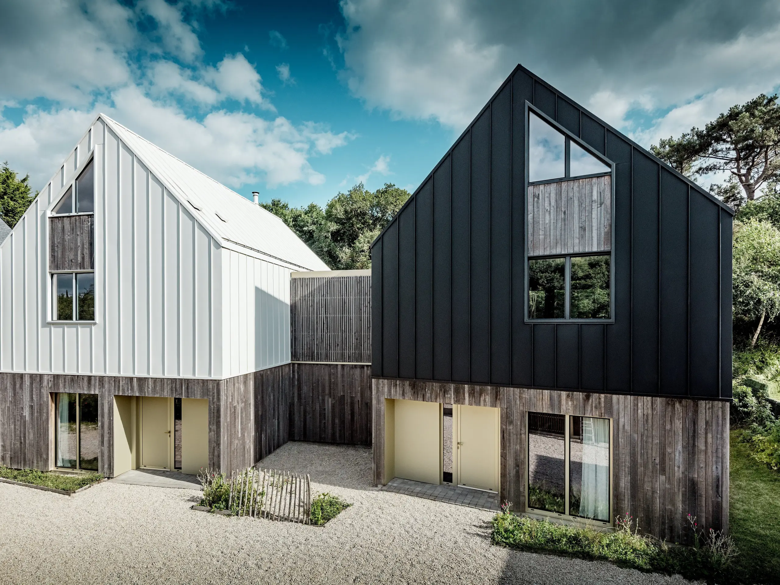 La façade du complexe résidentiel Le Rhune présente deux bâtiments modernes aux toits à deux pans remarquables et aux façades en aluminium PREFALZ contrastées, l'une blanche et l'autre gris-noir. Sur fond de ciel nuageux spectaculaire, les lignes épurées des façades à joints debout continus se détachent avec une élégance particulière. Inspirée des maisons traditionnelles de pêcheurs bretonnes, l'architecture allie les traditions architecturales régionales à un design contemporain. L'enveloppe du bâtiment, résistante et durable, en PREFALZ assure une liaison parfaite entre la toiture et la façade, permet des finitions précises et confère au complexe une allure moderne, haut de gamme et d'une beauté intemporelle.