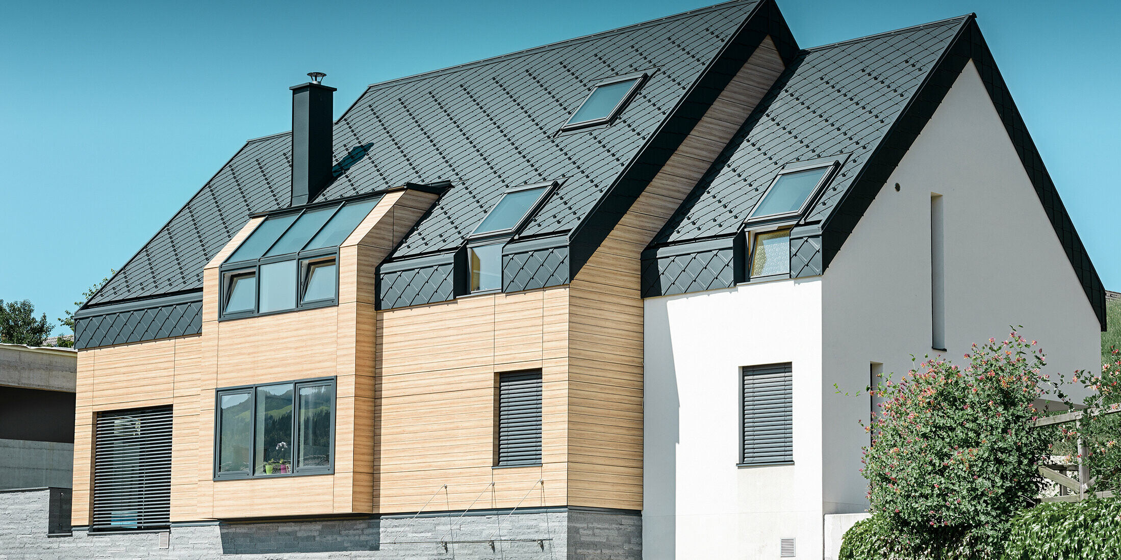 Nouvelle construction moderne avec un toit s’étendant jusqu’à la partie supérieure de la façade. Les losanges de toiture en aluminium couleur anthracite ont été utilisés pour la couverture