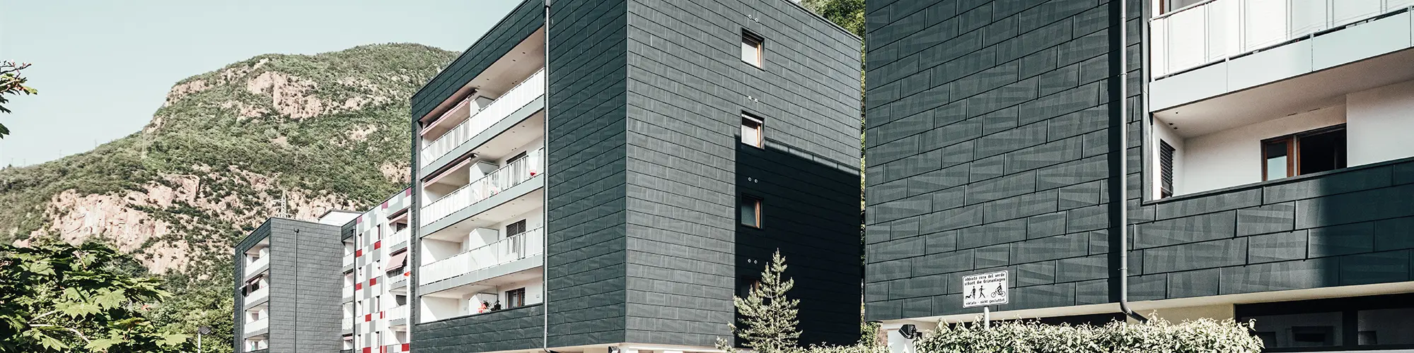 Vue de l'avancée du bâtiment rénové à Bozen. Les balcons avec leur balustrades blanches et la façade en panneaux de façade FX.12 Prefa.