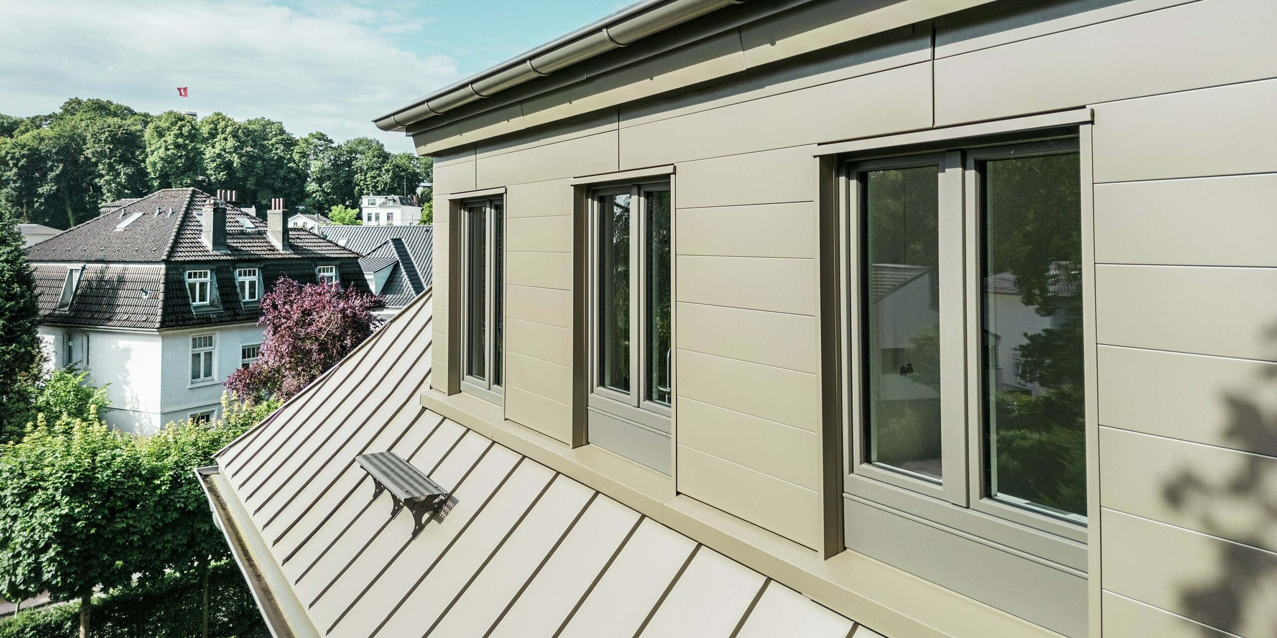 Vue détaillée de la Villa Blankenese à Hambourg, avec son élégante toiture PREFALZ et son bardage Siding PREFA couleur bronze. L'image met en valeur la pureté des lignes et la qualité de la fabrication en aluminium, garantissant durabilité et résistance aux intempéries. La finition bronze confère au bâtiment une allure sophistiquée et moderne, et crée des contrastes saisissants grâce aux grandes baies vitrées. Les produits PREFA offrent non seulement un design élégant, mais aussi une qualité sans entretien – la solution idéale pour une architecture exigeante, quel que soit l'environnement.