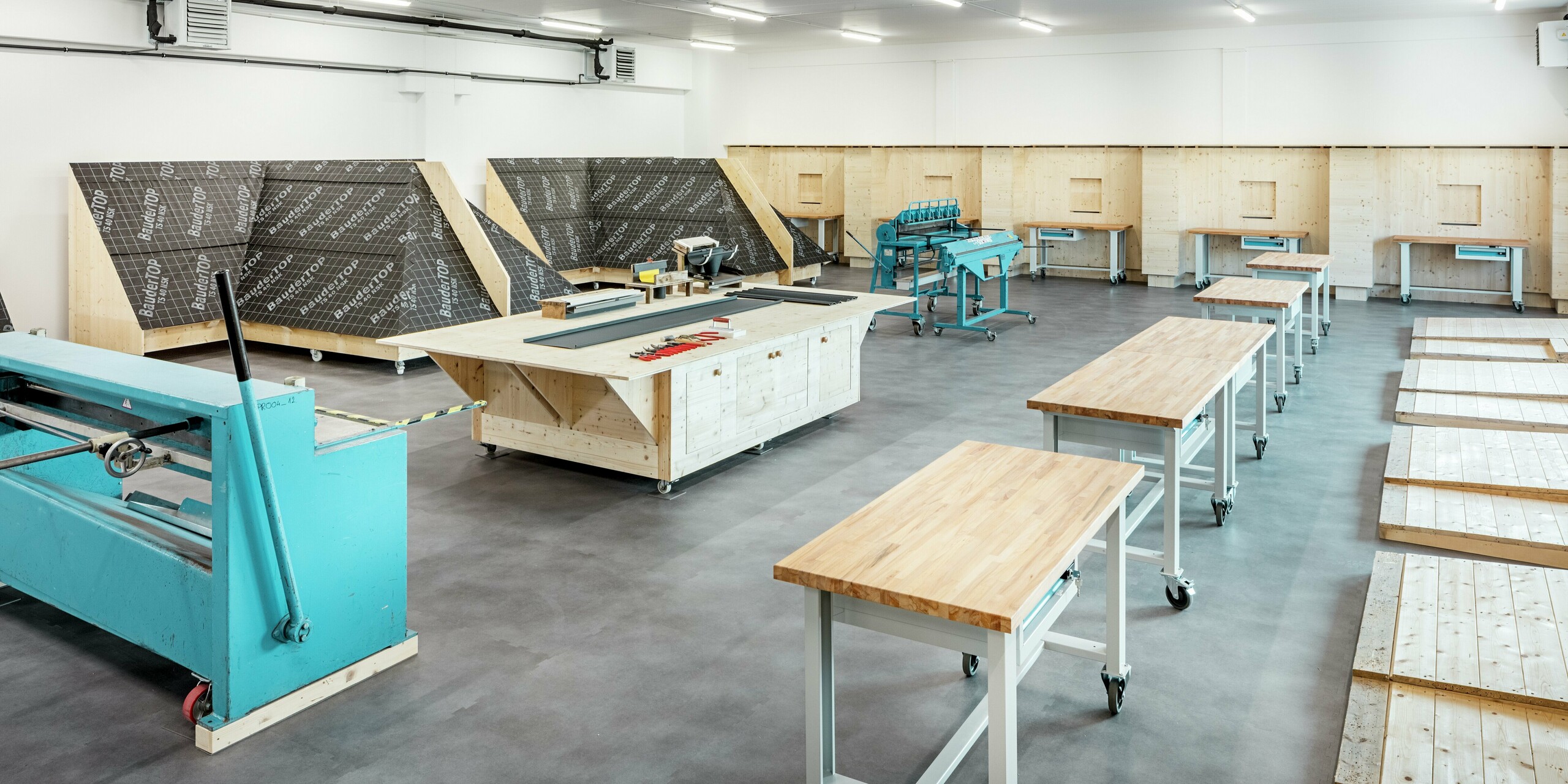 L'espace de formation pratique de la PREFA Academy de Törökbálint offre des conditions idéales pour la formation professionnelle et la formation continue. Equipée d'établis modernes, d'outils spéciaux et d'espaces de pratique, la salle permet une formation pratique des transformateurs. Ici, les professionnels apprennent à manipuler correctement les produits PREFA – de l'assemblage au traitement détaillé – directement sur des modèles réalistes.