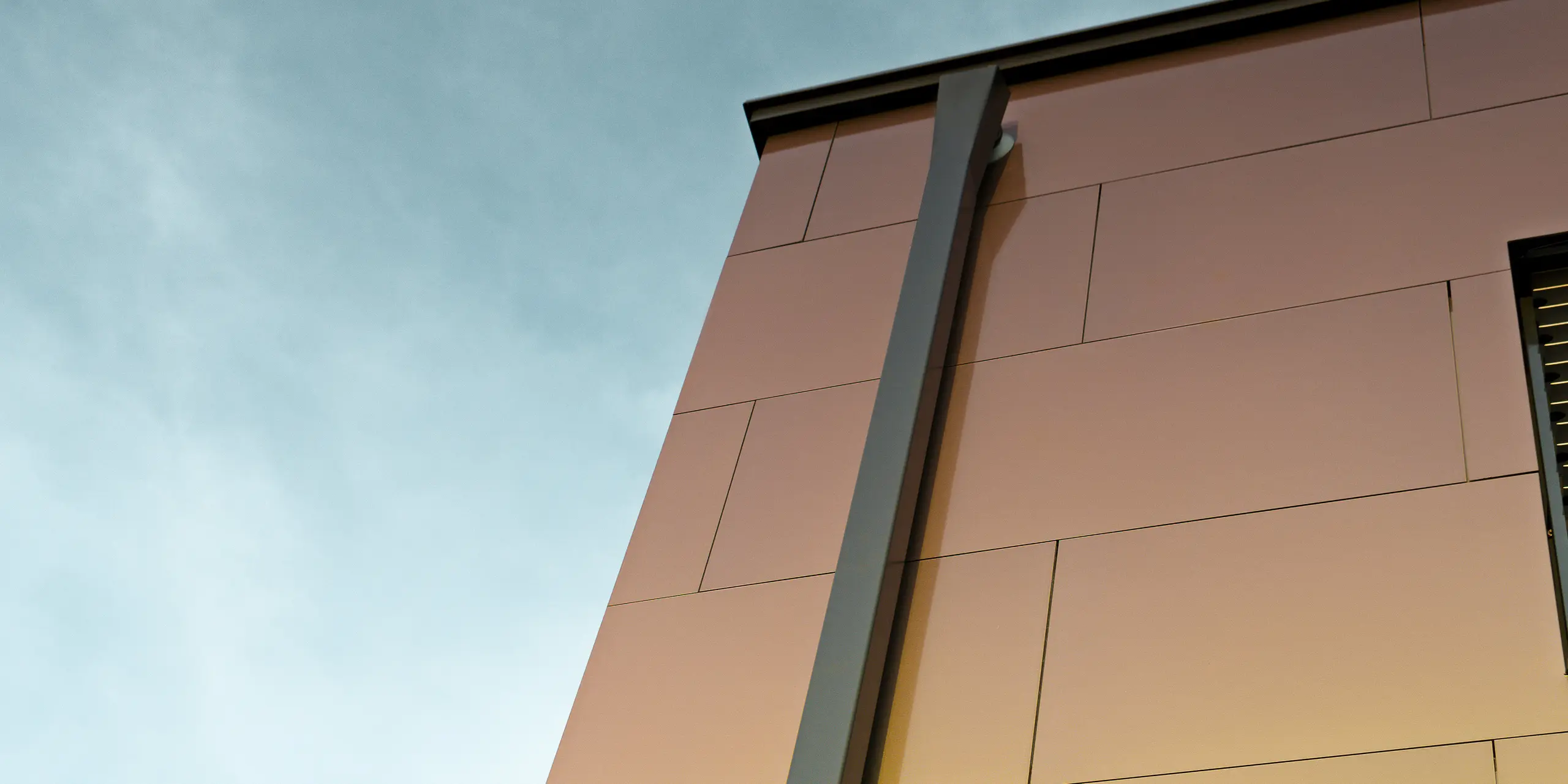Bordure d'une maison individuelle moderne avec le tuyau de descente carré PREFA moderne pour l'évacuation des eaux pluviales du toit plat. La façade est revêtue d'un panneau composite en aluminium dans la couleur chatoyante « spring lake ».