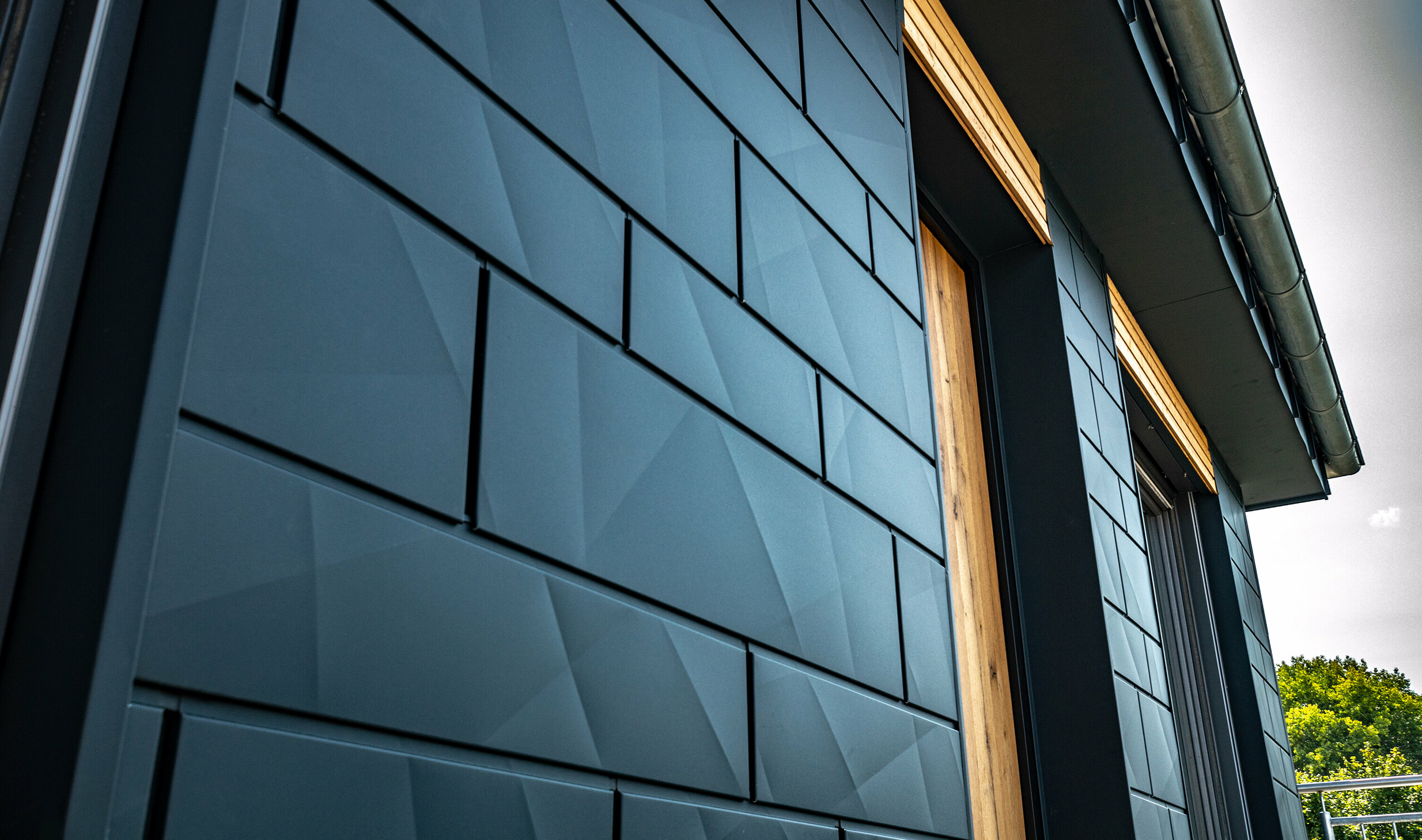 Façade avec Siding.X PREFA couleur anthracite avec portes de balcon et grandes surfaces vitrées mélangées avec un habillage en bois.