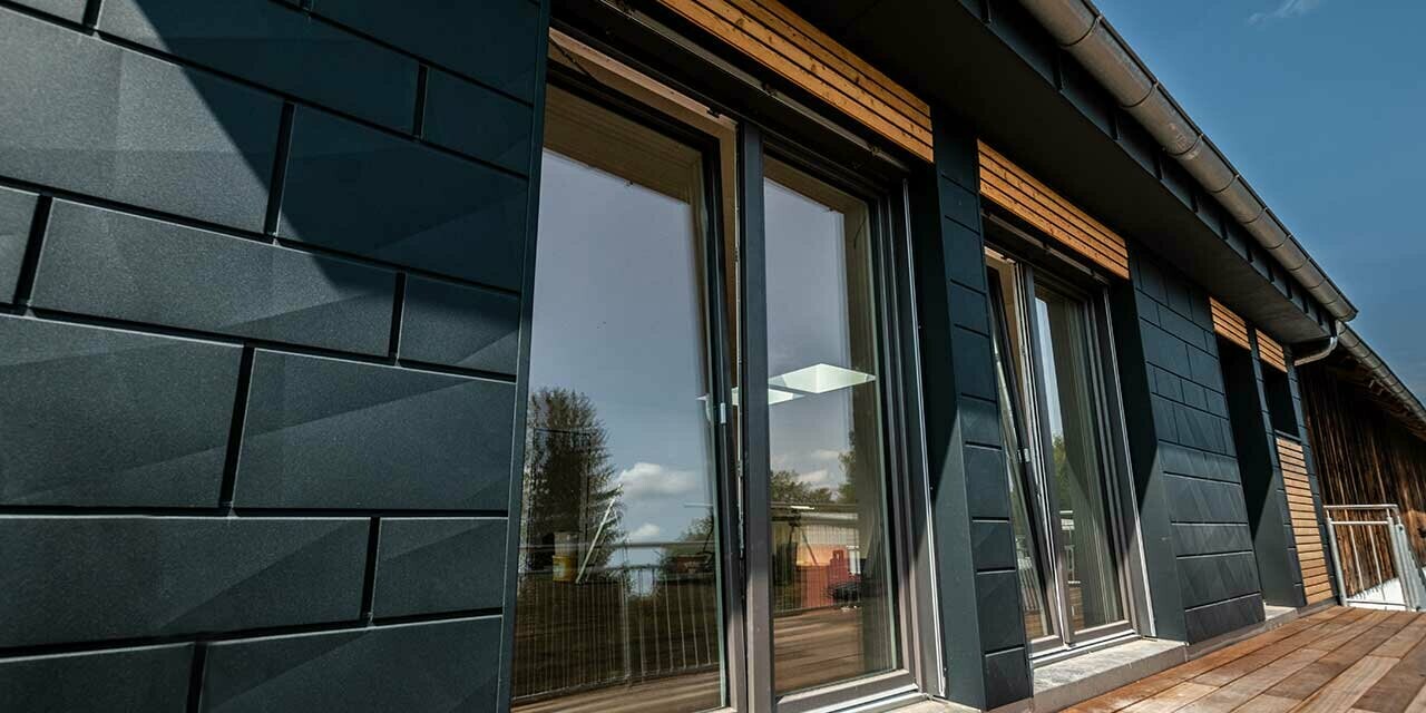 Façade avec Siding.X PREFA couleur anthracite avec portes de balcon et grandes surfaces vitrées mélangées avec un habillage en bois.