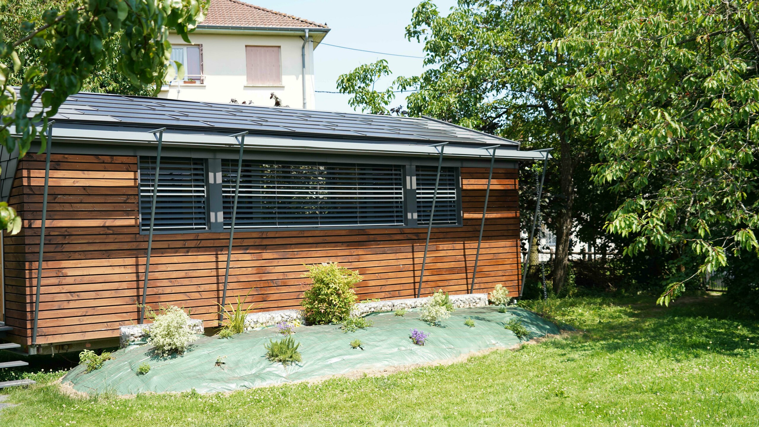 Prise de vue de face du projet de bureau mobile réalisé par l'architecte Audrey Lablanche. On aperçoit une façade en bois, de grandes fenêtre pour laisser passer la lumière et une toiture en tuile solaire PREFA