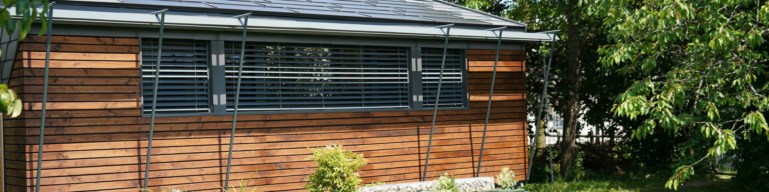 Prise de vue de face du projet de bureau mobile réalisé par l'architecte Audrey Lablanche. On aperçoit une façade en bois, de grandes fenêtre pour laisser passer la lumière et une toiture en tuile solaire PREFA