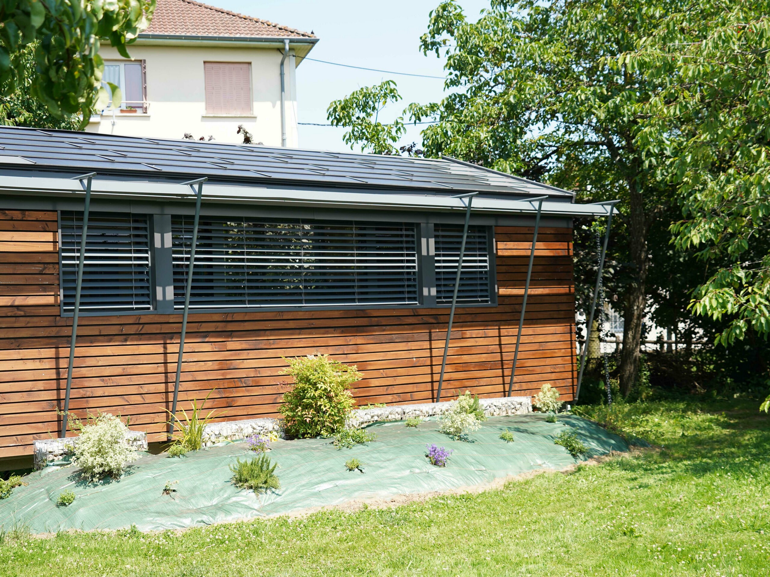 Prise de vue de face du projet de bureau mobile réalisé par l'architecte Audrey Lablanche. On aperçoit une façade en bois, de grandes fenêtre pour laisser passer la lumière et une toiture en tuile solaire PREFA
