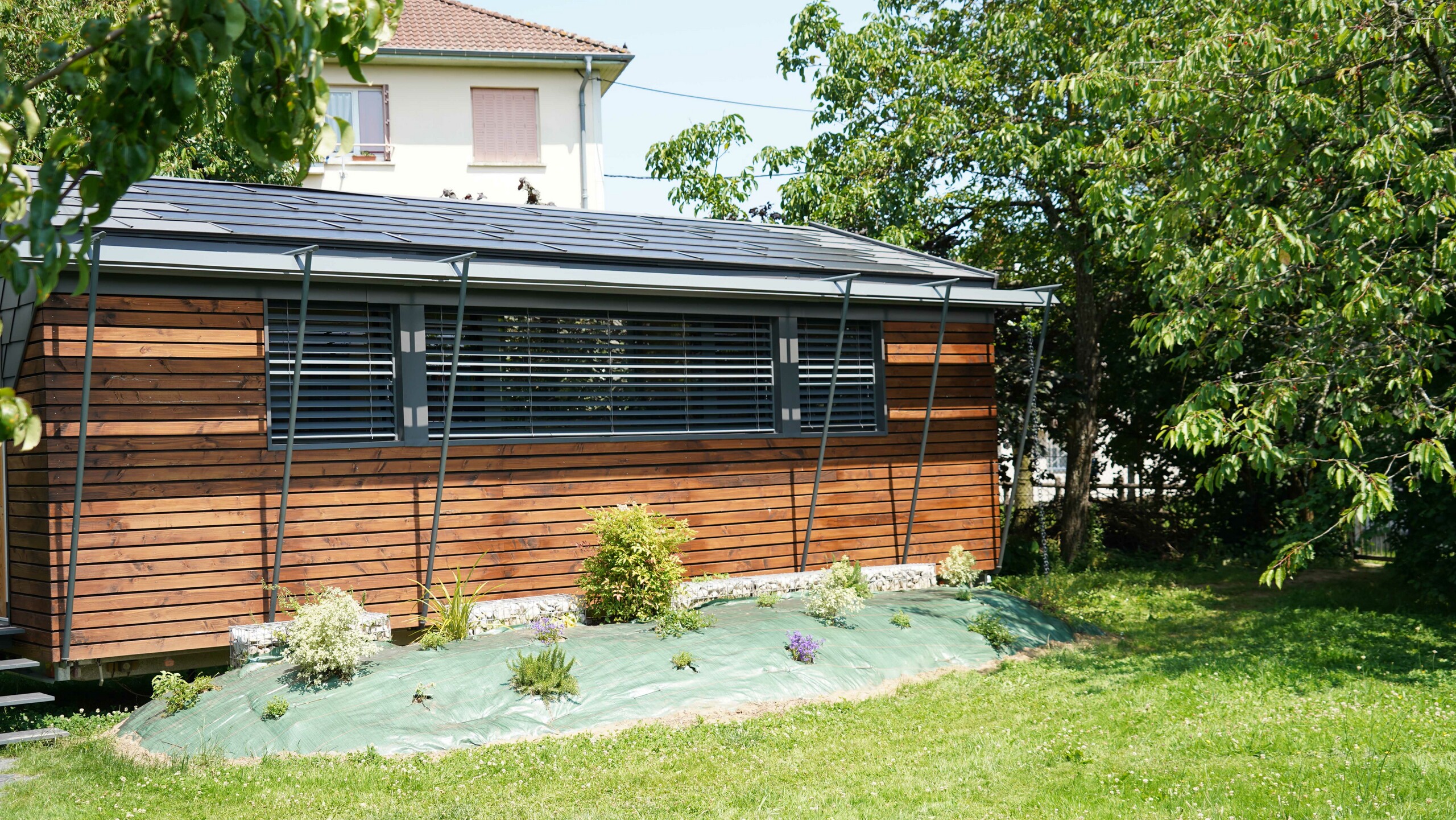 Prise de vue de face du projet de bureau mobile réalisé par l'architecte Audrey Lablanche. On aperçoit une façade en bois, de grandes fenêtre pour laisser passer la lumière et une toiture en tuile solaire PREFA