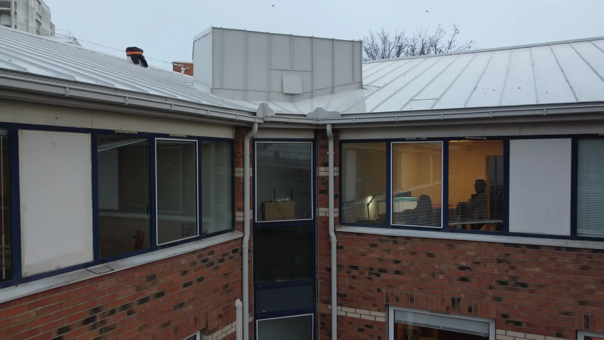 Vue de face du bâtiment où l'on voit le mariage de deux matériaux : l'aluminium et la brique