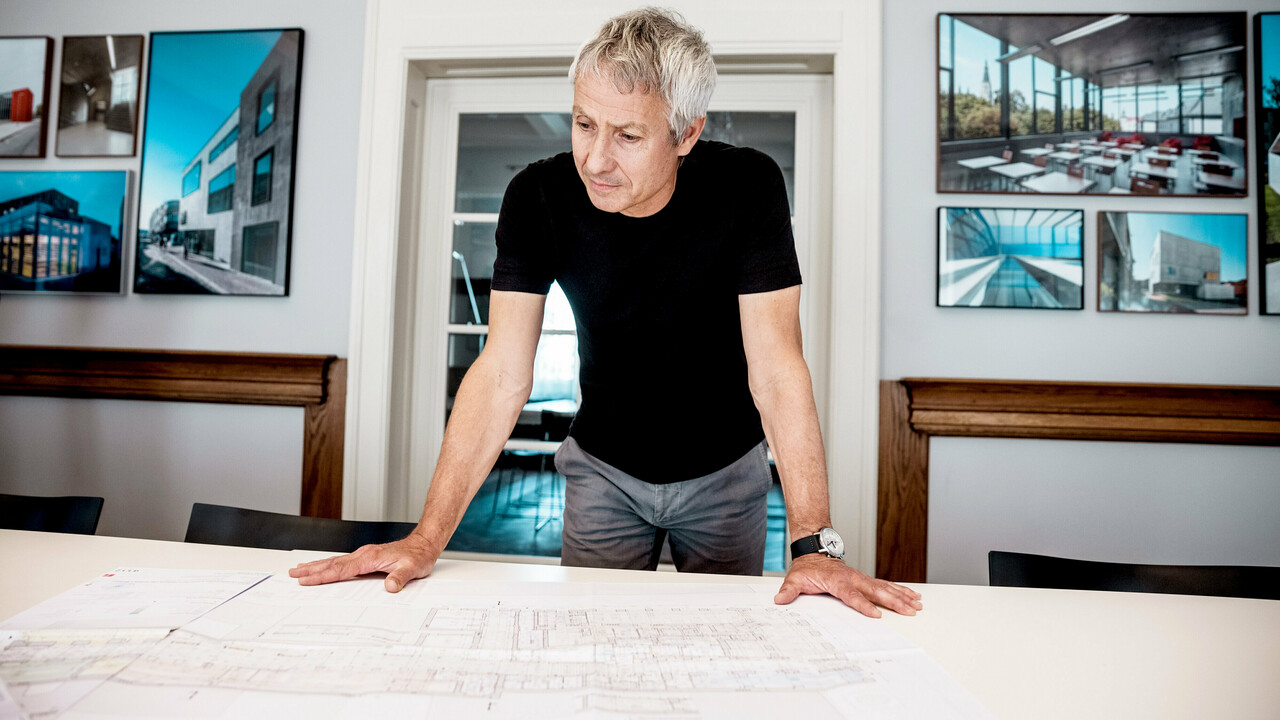 Un architecte travaille sur des plans de construction détaillés dans un bureau moderne, entouré de photos impressionnantes de projets architecturaux PREFA.