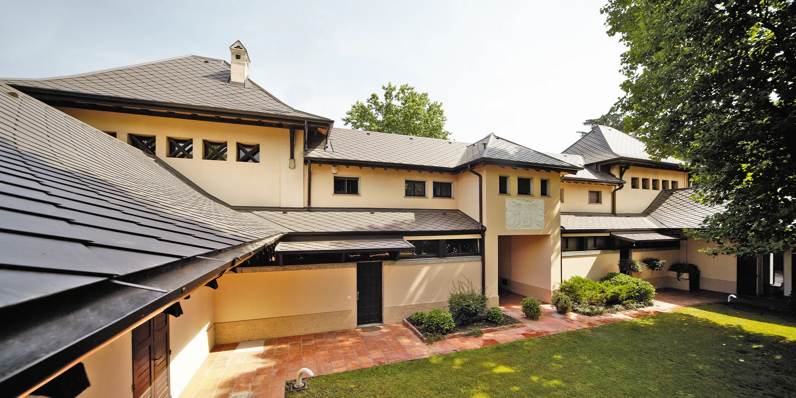 Villa italienne avec un toit en losanges couleur P.10 brun de PREFA, avec façade beige et cour intérieure ombragée