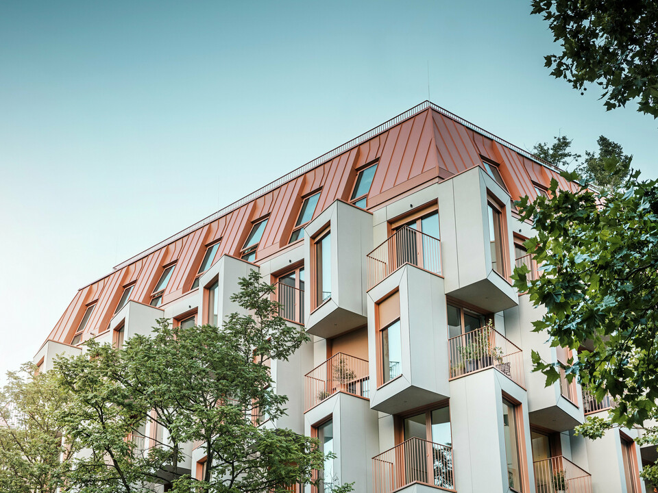 Architecture résidentielle moderne dans le projet Van B à Munich avec une façade en baie vitrée innovante et un toit en aluminium PREFALZ remarquable dans la couleur spéciale IGP Orange HDP de PREFA. Le matériau de toiture de haute qualité impressionne par son extrême durabilité, sa grande résistance et sa solidité des couleurs. En combinaison avec la conception cubique de la façade et les grandes surfaces vitrées, une image globale harmonieuse est créée qui combine fonctionnalité, design et durabilité au plus haut niveau - idéal pour la vie urbaine.