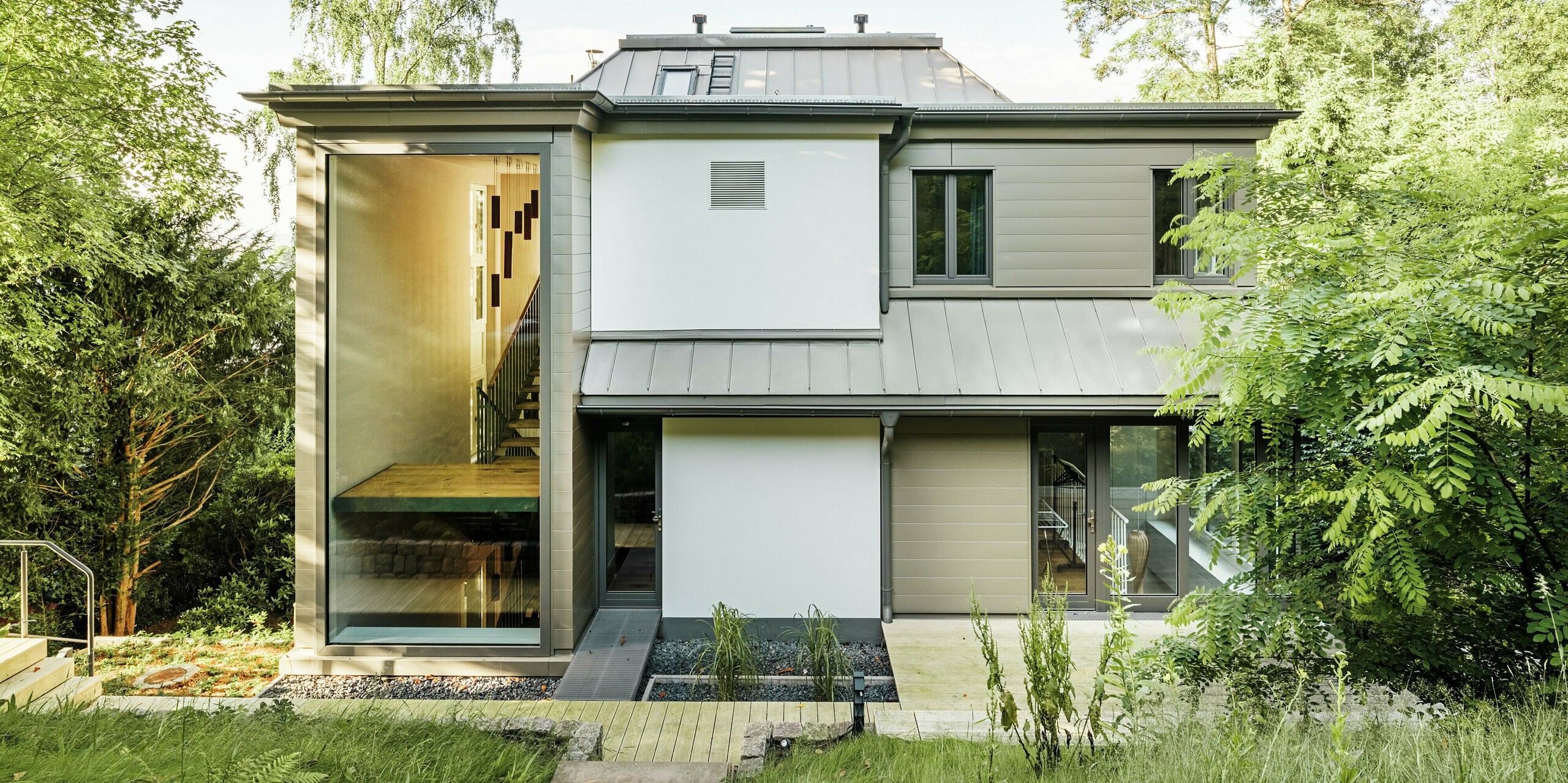 L'image présente la façade arrière de la Villa Blankenese à Hambourg, caractérisée par une architecture moderne et épurée. Le bardage PREFA couleur bronze est particulièrement remarquable et confère à la façade une élégance intemporelle. La toiture, revêtue de PREFALZ couleur bronze, s'intègre harmonieusement à l'ensemble. De larges surfaces vitrées et l'alliance de l'aluminium et du plâtre soulignent le caractère haut de gamme du bâtiment. Durables, les produits PREFA offrent non seulement un design raffiné, mais aussi une résistance maximale aux intempéries et ne nécessitent aucun entretien.