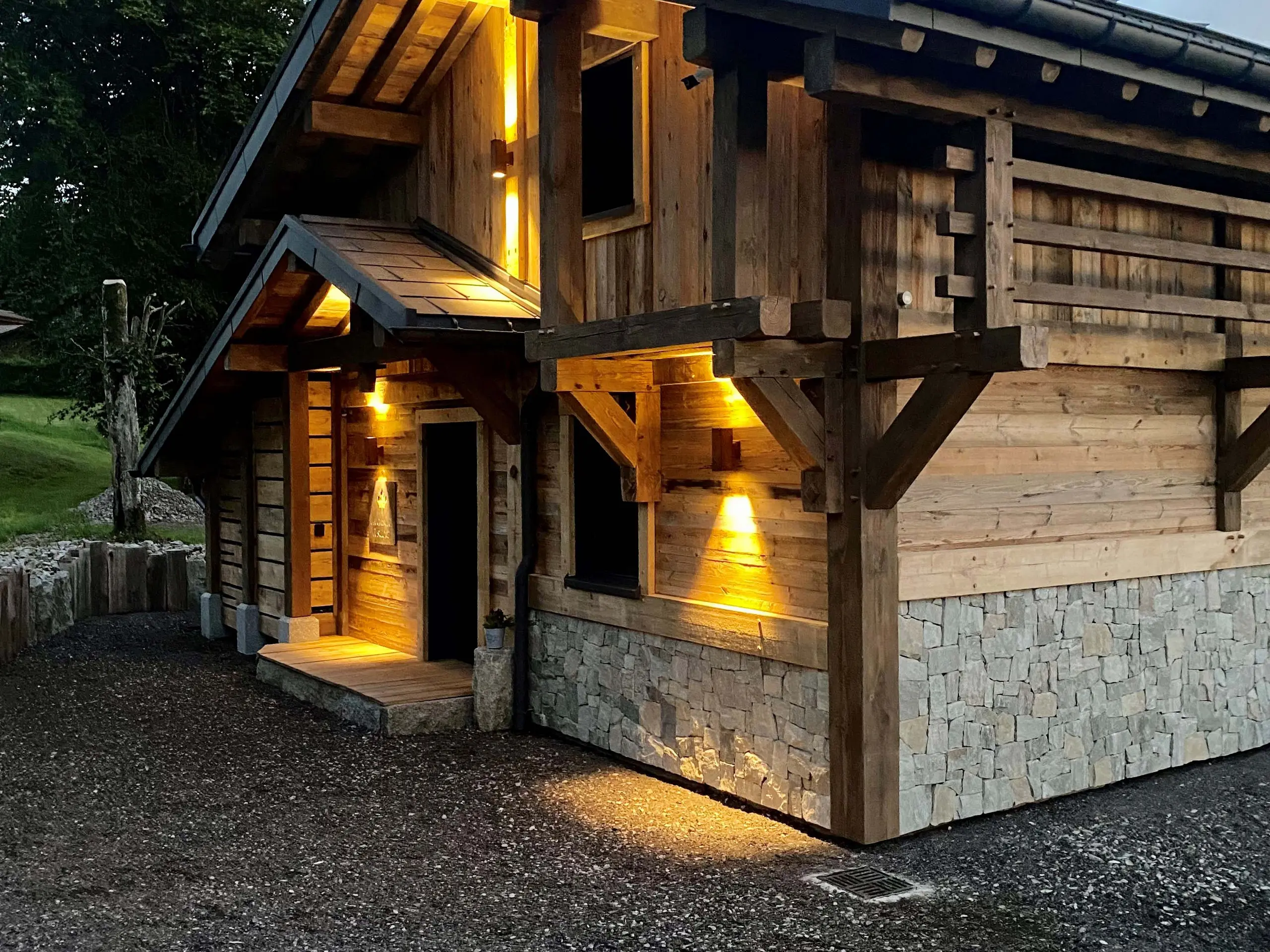 Vue de l'entrée du gîte La Cabane à Sucre dont les luminaires créent de jolis jeux de lumière et mettent en avant la façade en bois