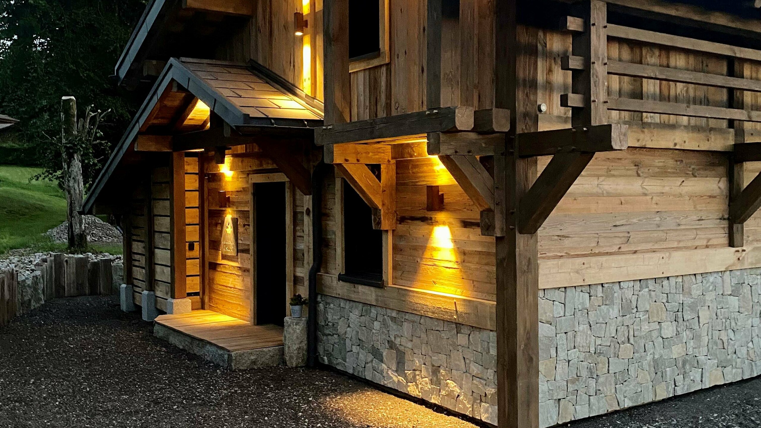 Vue de l'entrée du gîte La Cabane à Sucre dont les luminaires créent de jolis jeux de lumière et mettent en avant la façade en bois