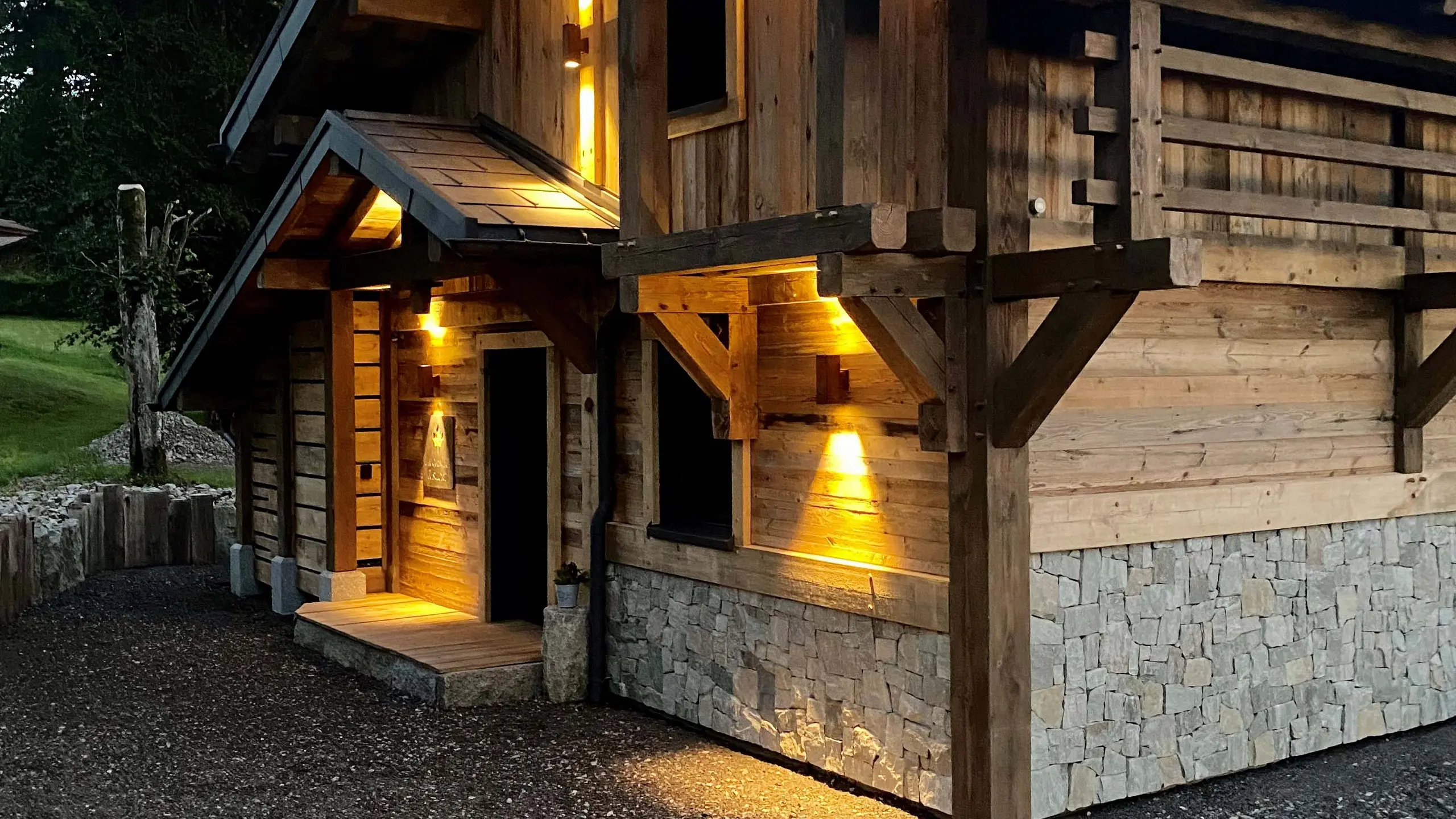 Vue de l'entrée du gîte La Cabane à Sucre dont les luminaires créent de jolis jeux de lumière et mettent en avant la façade en bois