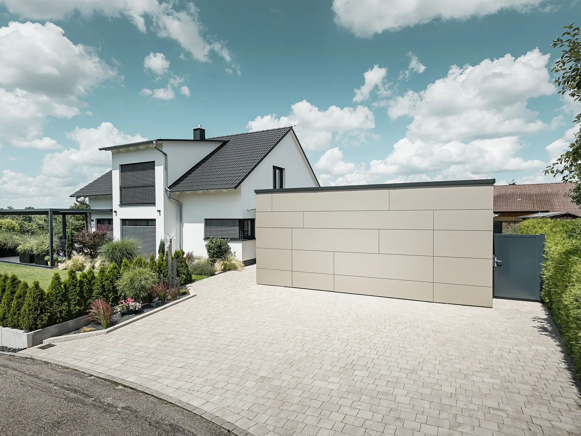 La façade du garage de cette maison individuelle est entièrement revêtue avec le panneau composite en aluminium couleur bronze. On ne distingue pas non plus la porte de garage des joints. Une allée spacieuse s'étend juste devant.