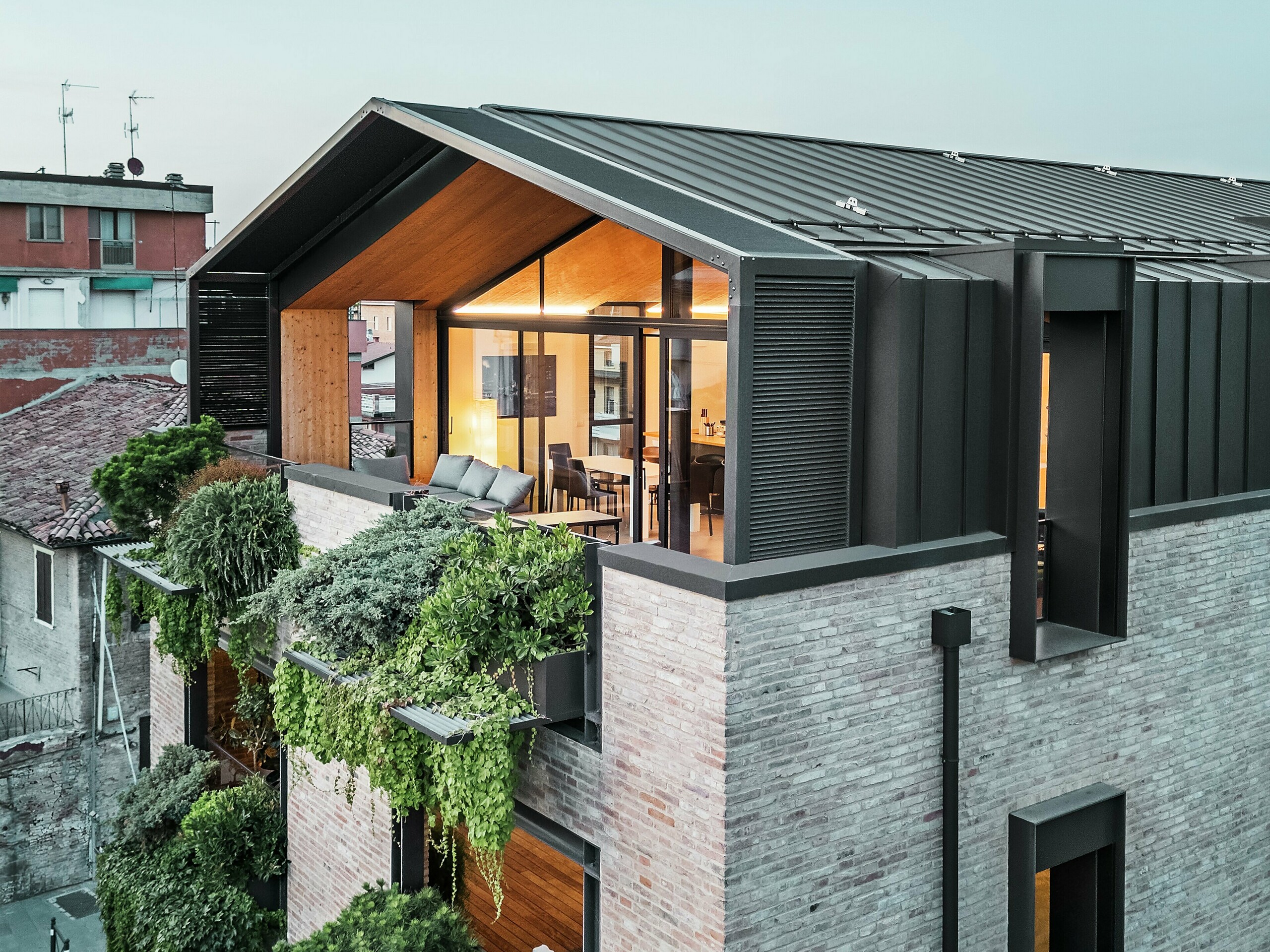 Maison moderne en Italie avec toiture en aluminium PREFALZ en P.10 brun noisette, grandes surfaces vitrées, façade végétalisée et construction en briques – une alliance réussie entre durabilité et architecture contemporaine.